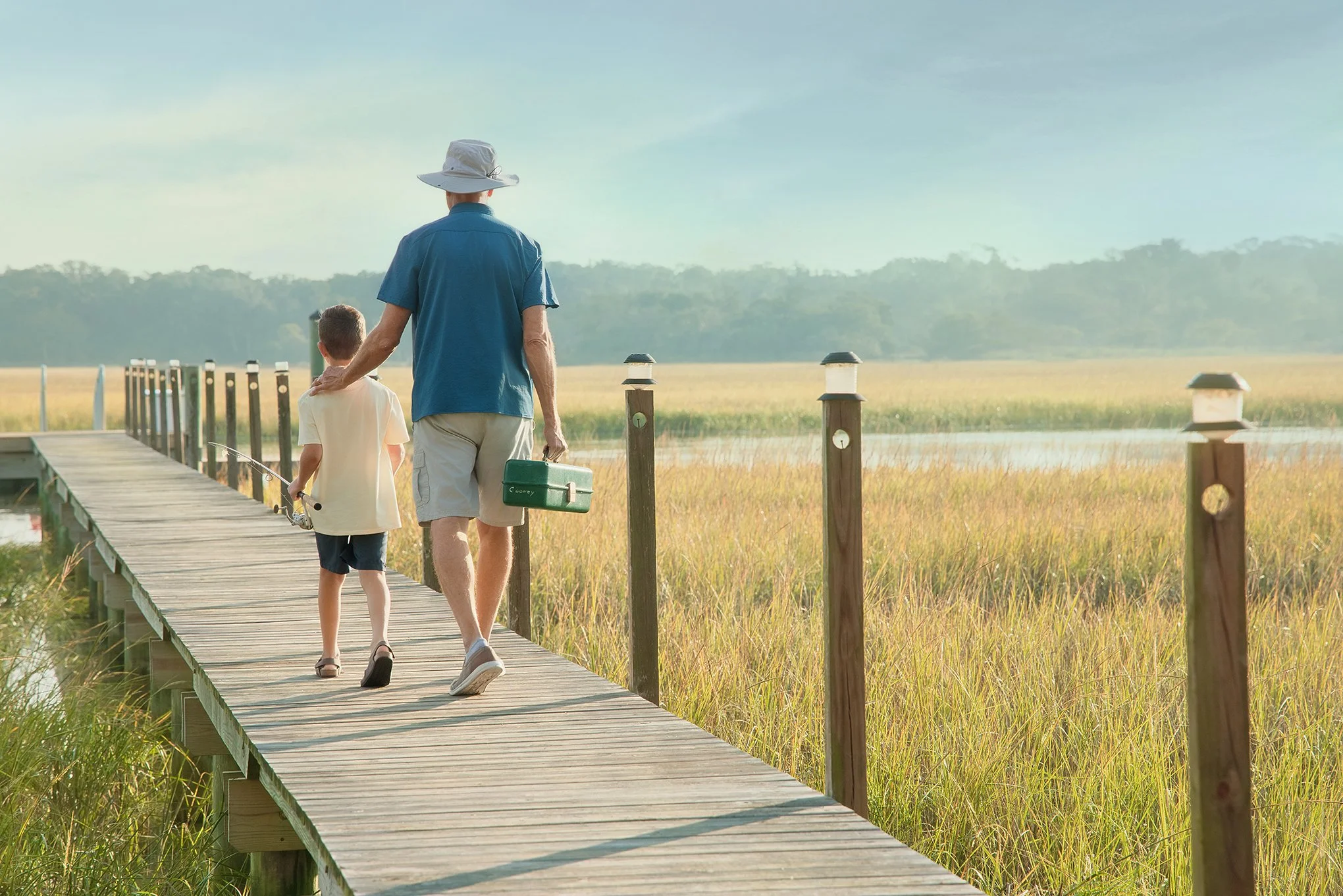 Father and son carrying fishing gear along a dock through the coastal marshes of Amelia Island, Florida.