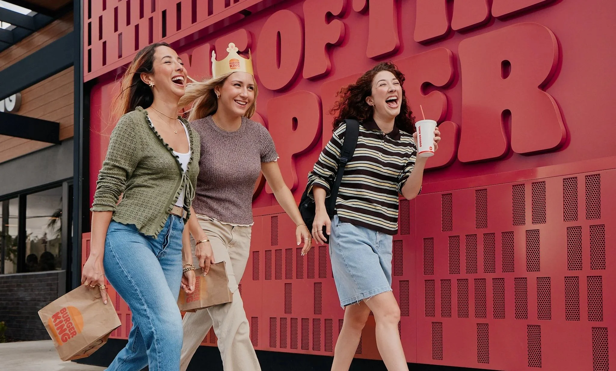 Three women walking outside Burger King in front of the red Home of the Whopper wall.