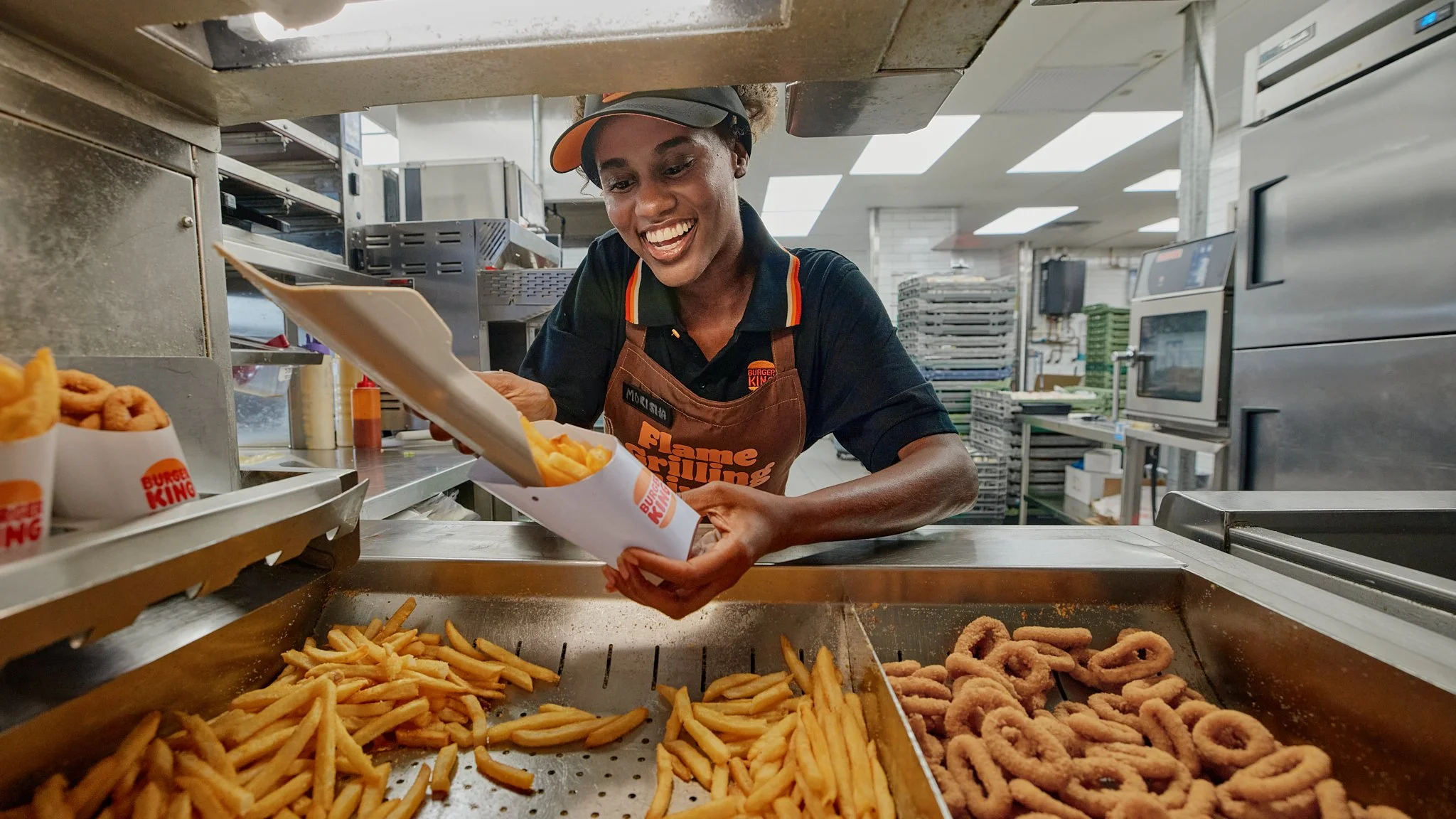 Burger King employee filling an order with fries in the restaurant kitchen.