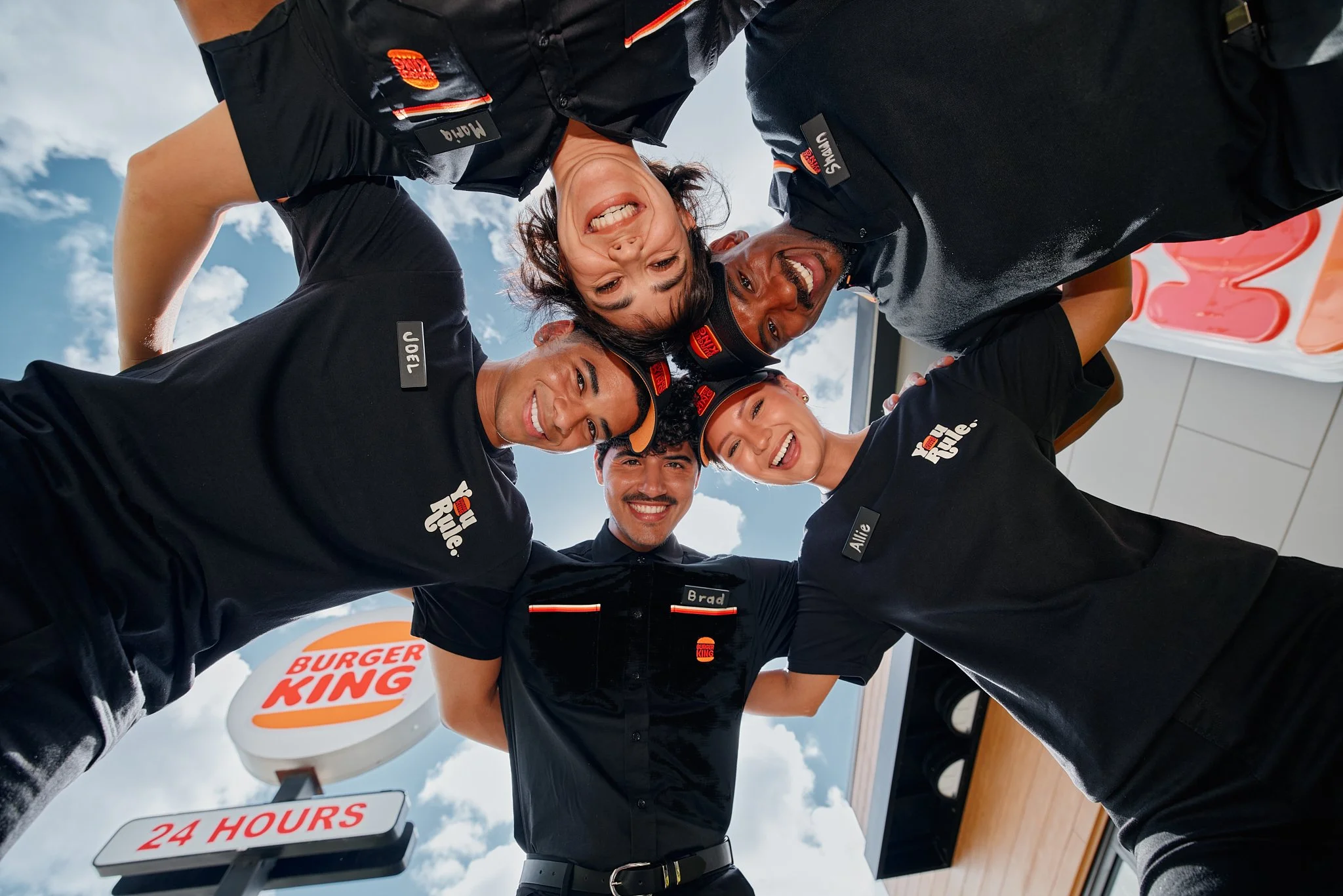 Burger King employees leaning into a team huddle and smiling down toward the camera