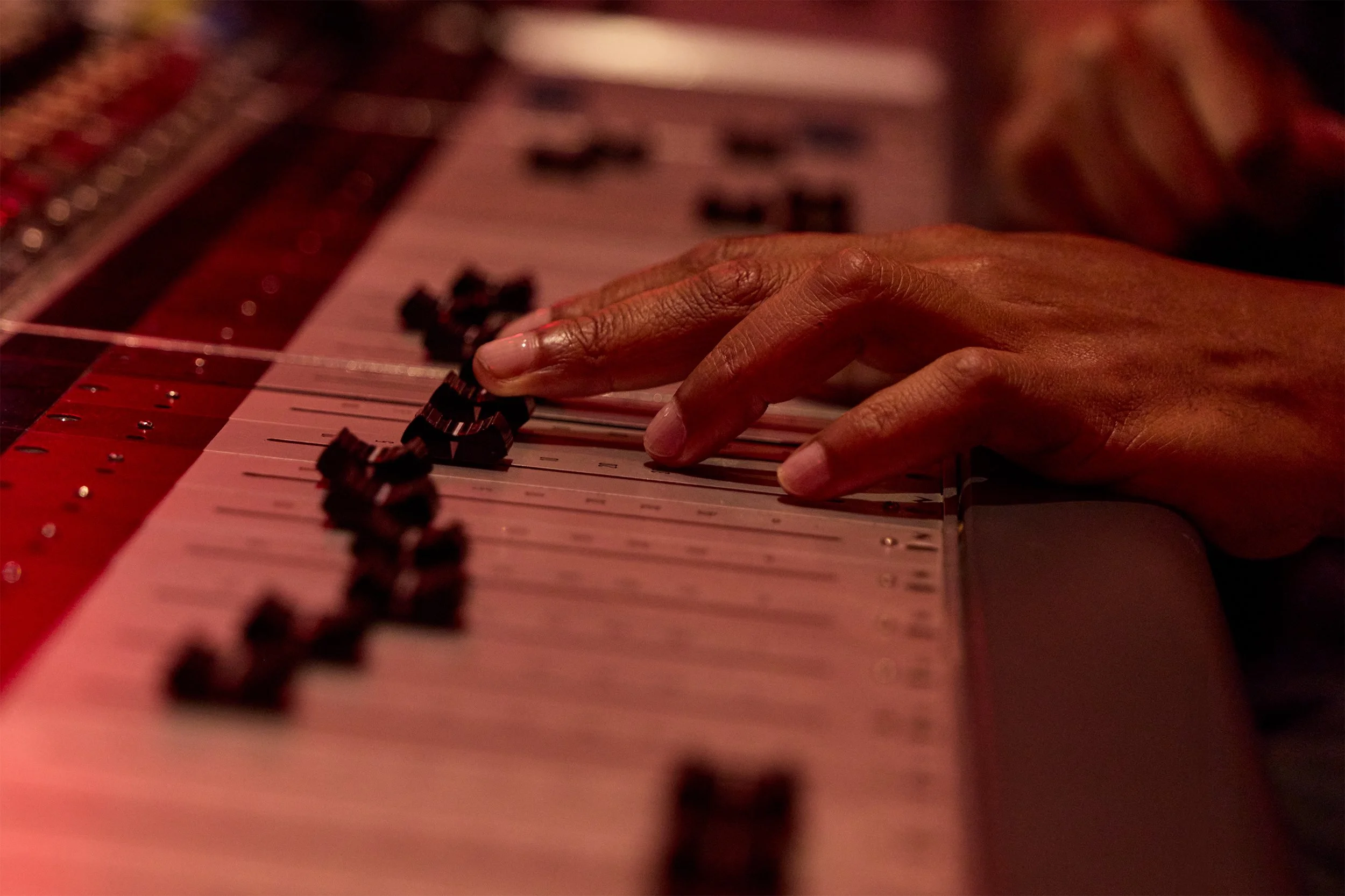 Timbaland’s hand adjusting faders on a professional recording studio mixing console.
