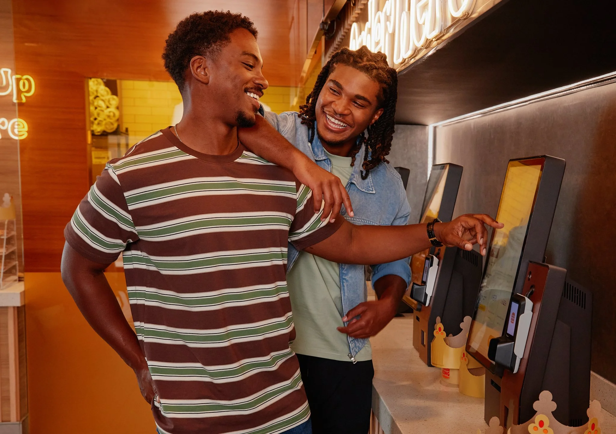 Two friends laughing together while using a Burger King self-order kiosk.