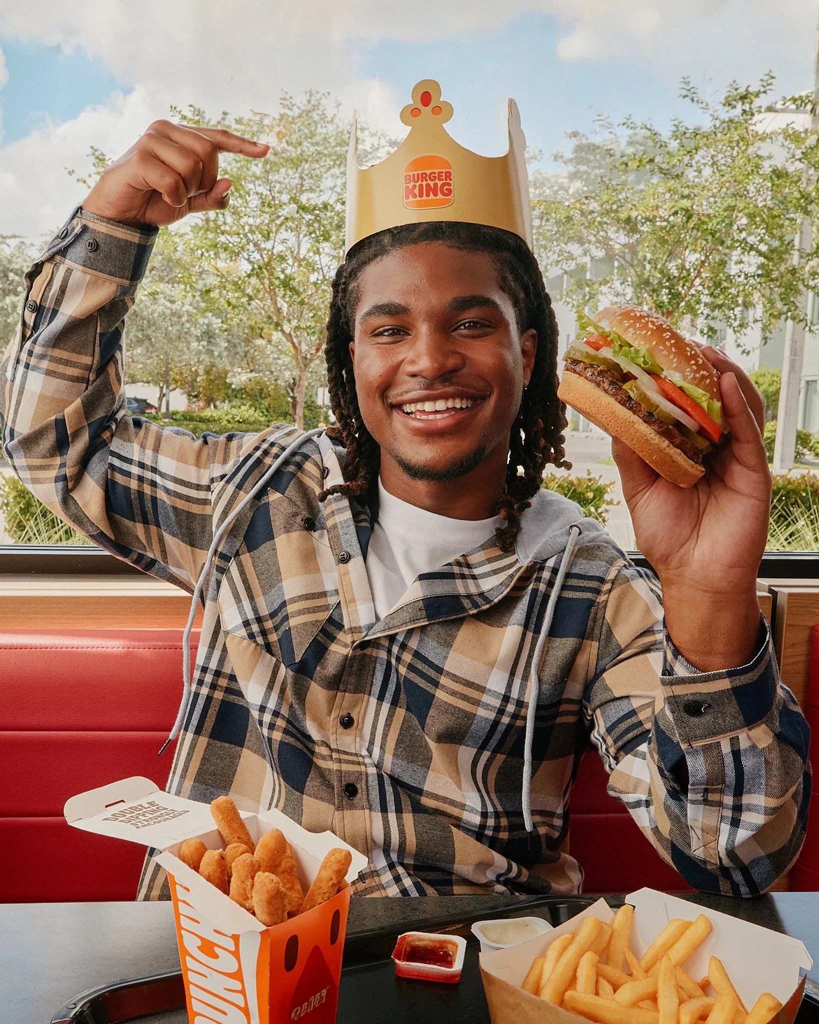Young man wearing a Burger King crown and holding a burger at a restaurant table.
