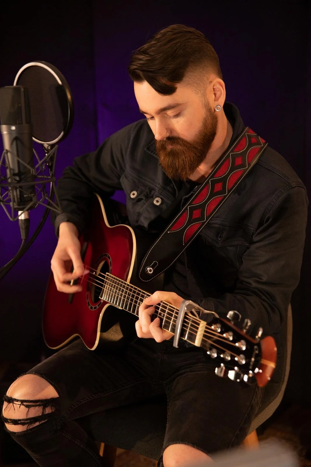 Man with beard playing acoustic guitar near microphone