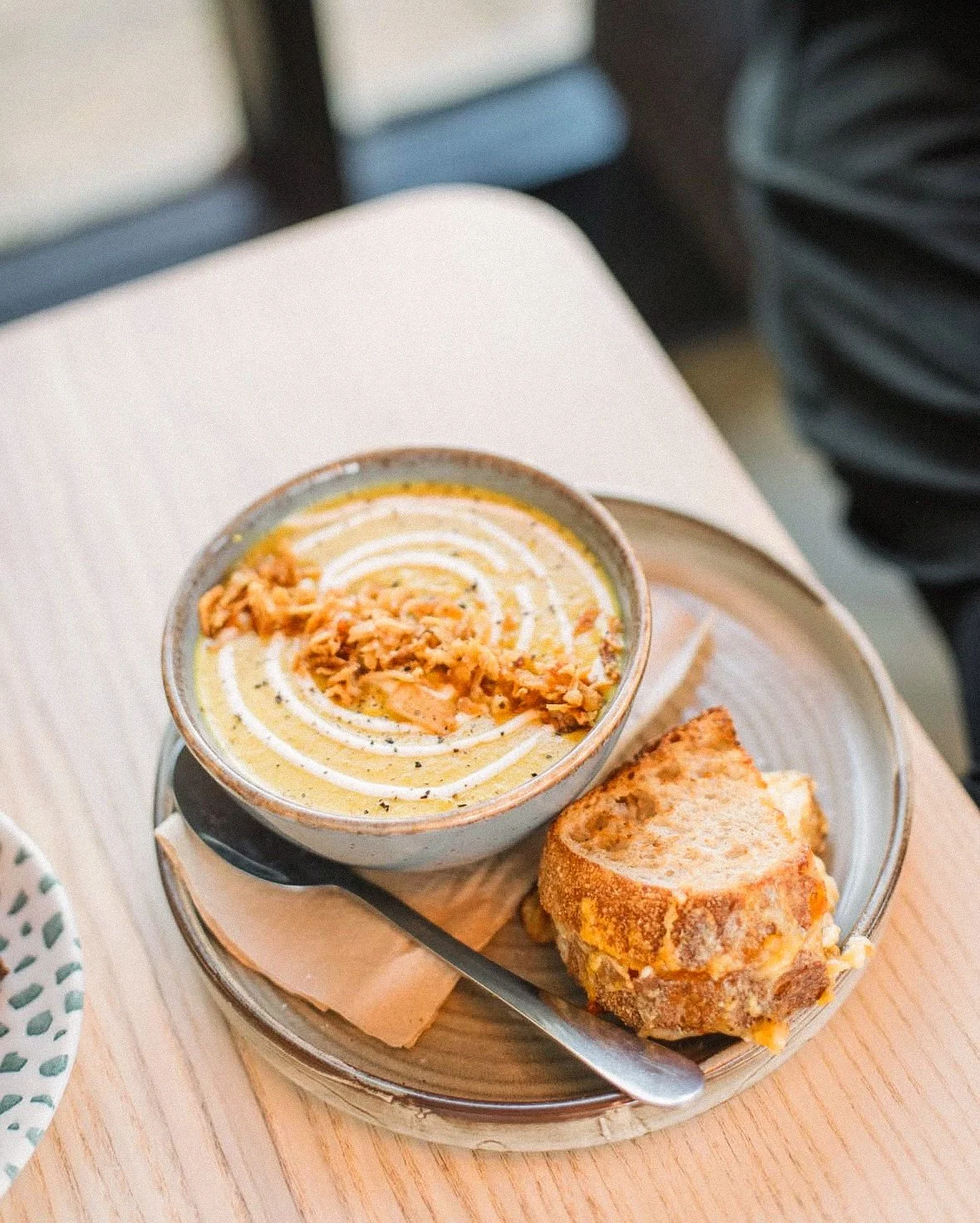 A bowl of creamy soup garnished with shredded cheese and black pepper, served with a side of toasted bread on a plate.