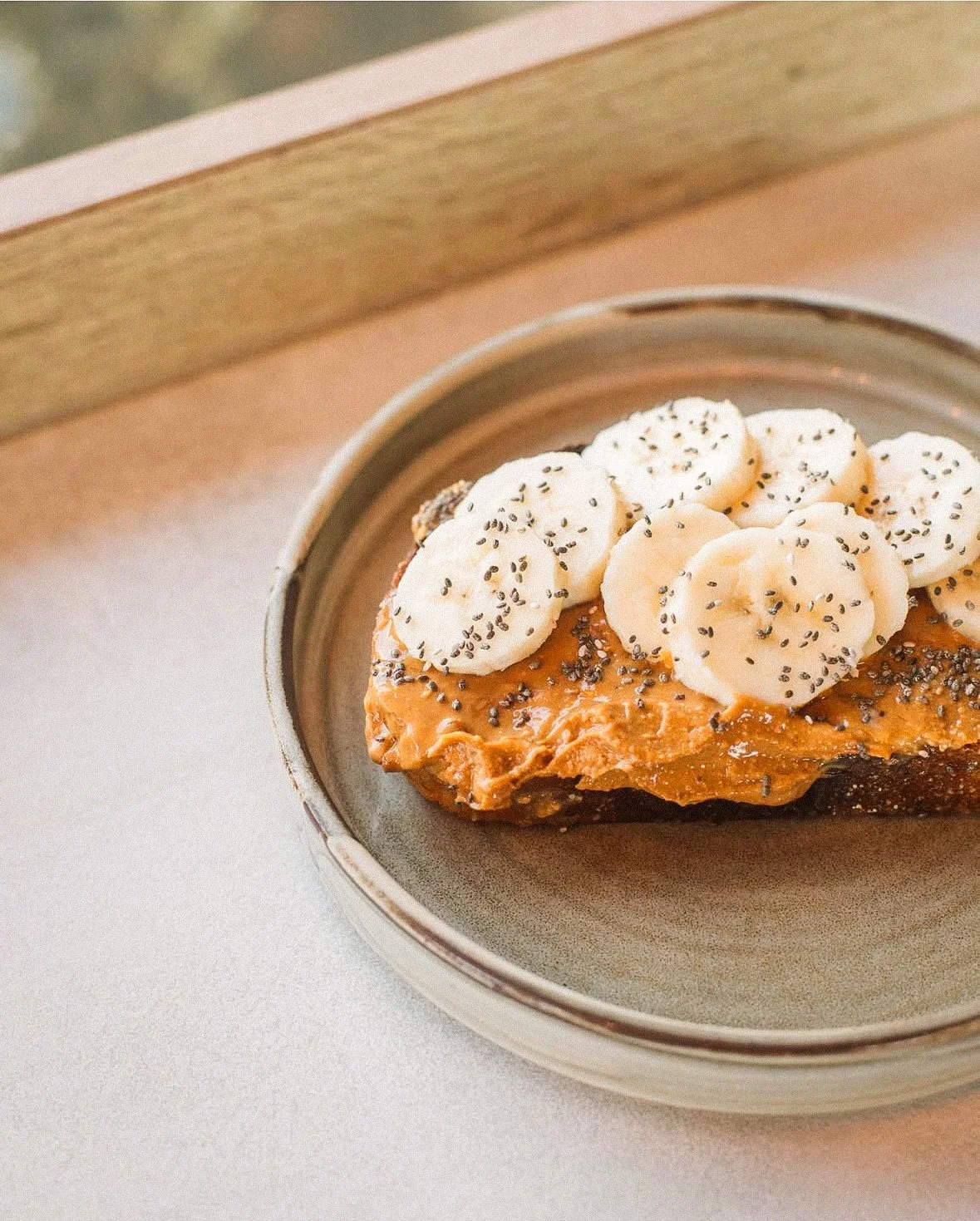 Sliced banana atop caramelized toast sprinkled with chia seeds on a ceramic plate.