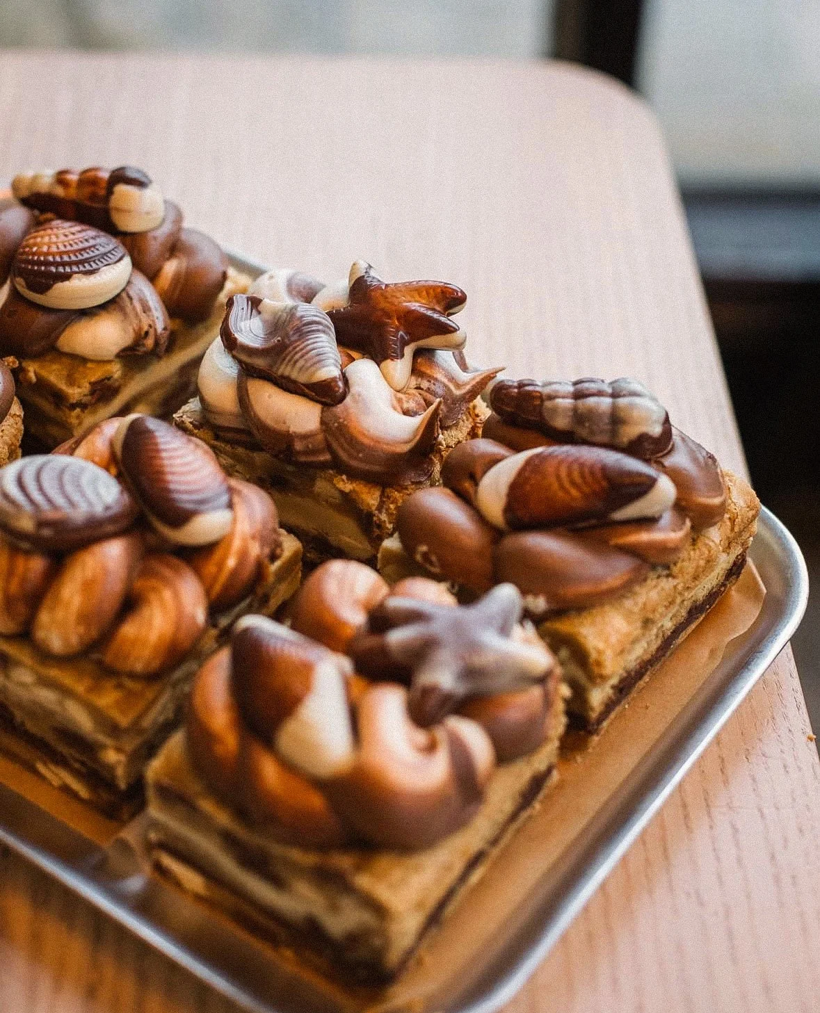 Close-up of multiple chocolate-topped pastries on a metal tray, featuring various shapes and swirls of milk, dark, and white chocolate.
