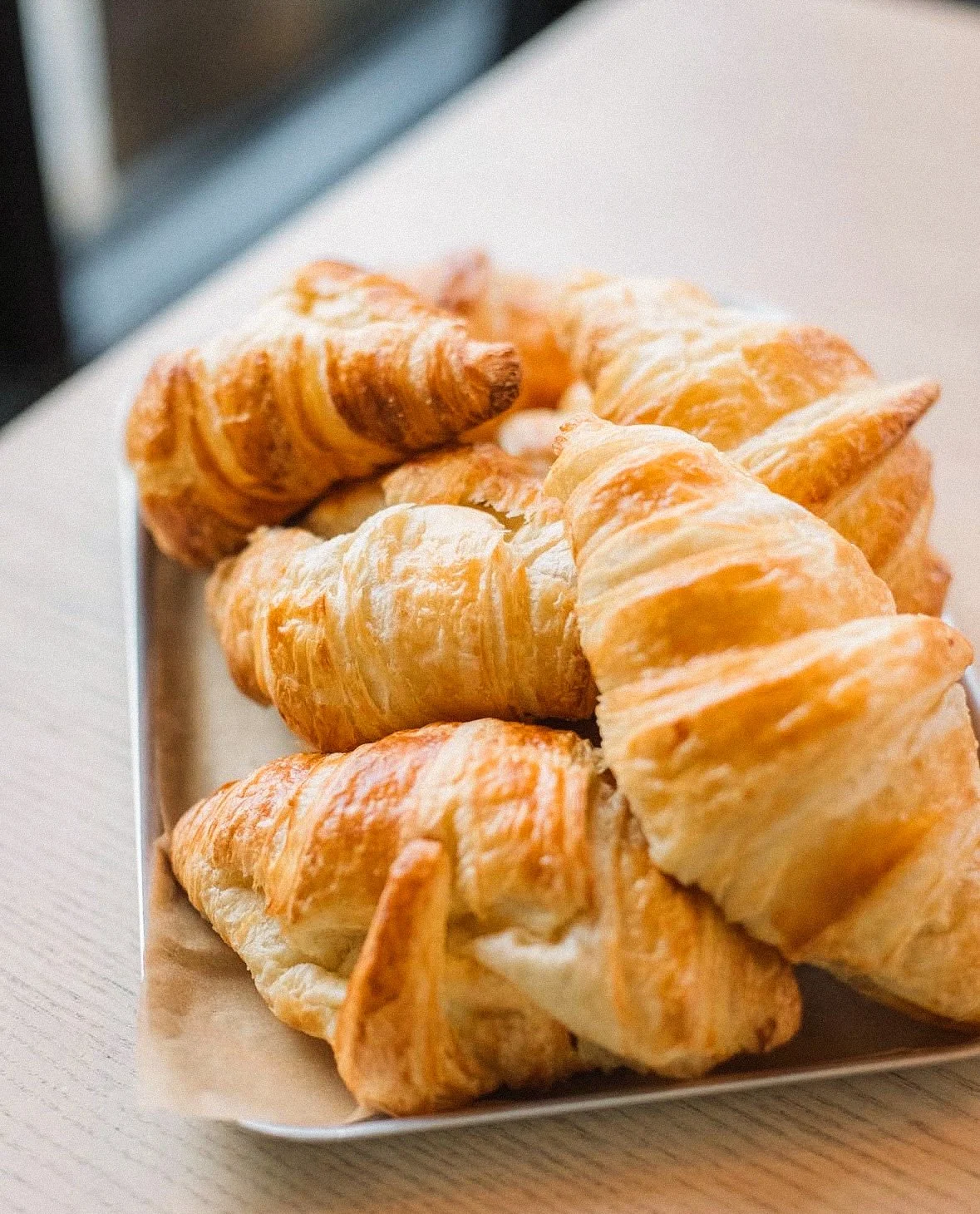 A plate of golden-brown croissants stacked on a white tray.