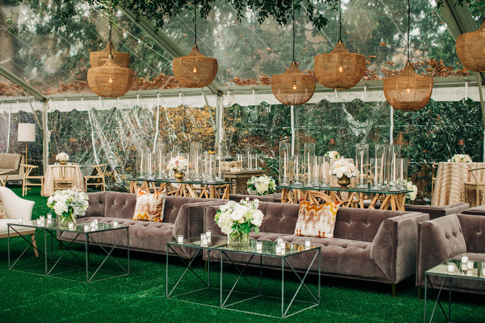 a tented reception area with glass tables, chandeliers, and couches