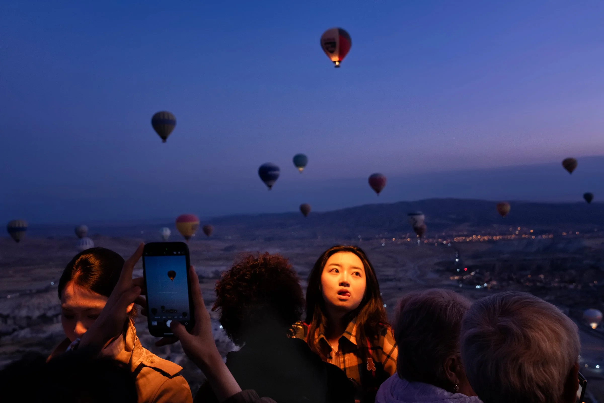  NYC Exhibition, 2026  In Kapadokya’s enchanted dawn, the balloon’s flame lights up passengers’ faces. The elderly, captivated by the timeless landscape, live in the moment, while the young, caught in technology’s divide, rush to capture selfies in i