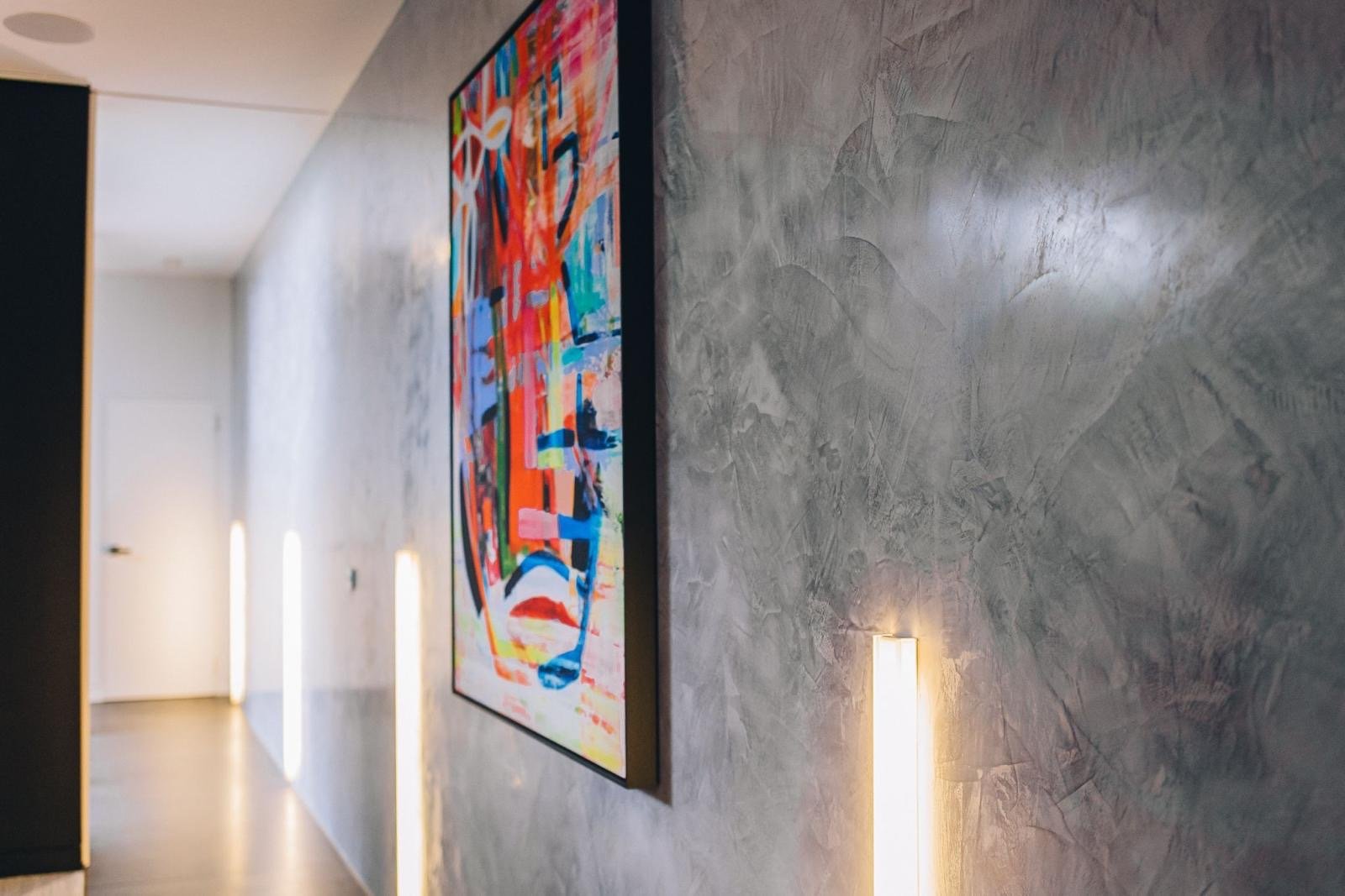 Textured plaster corridor with artwork and vertical wall lighting