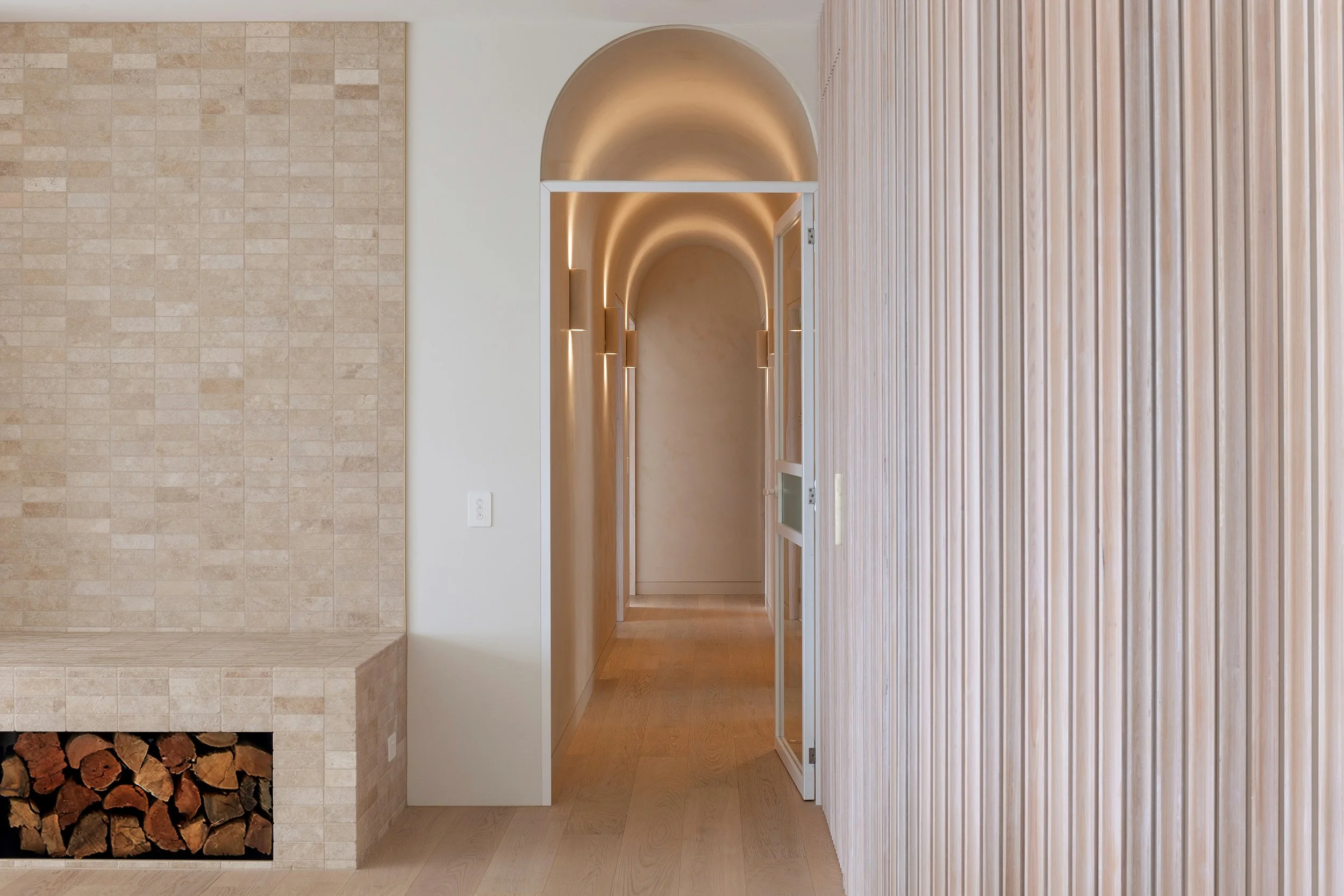 Arched hallway at Dromana residence with soft integrated wall lighting and warm plaster finish