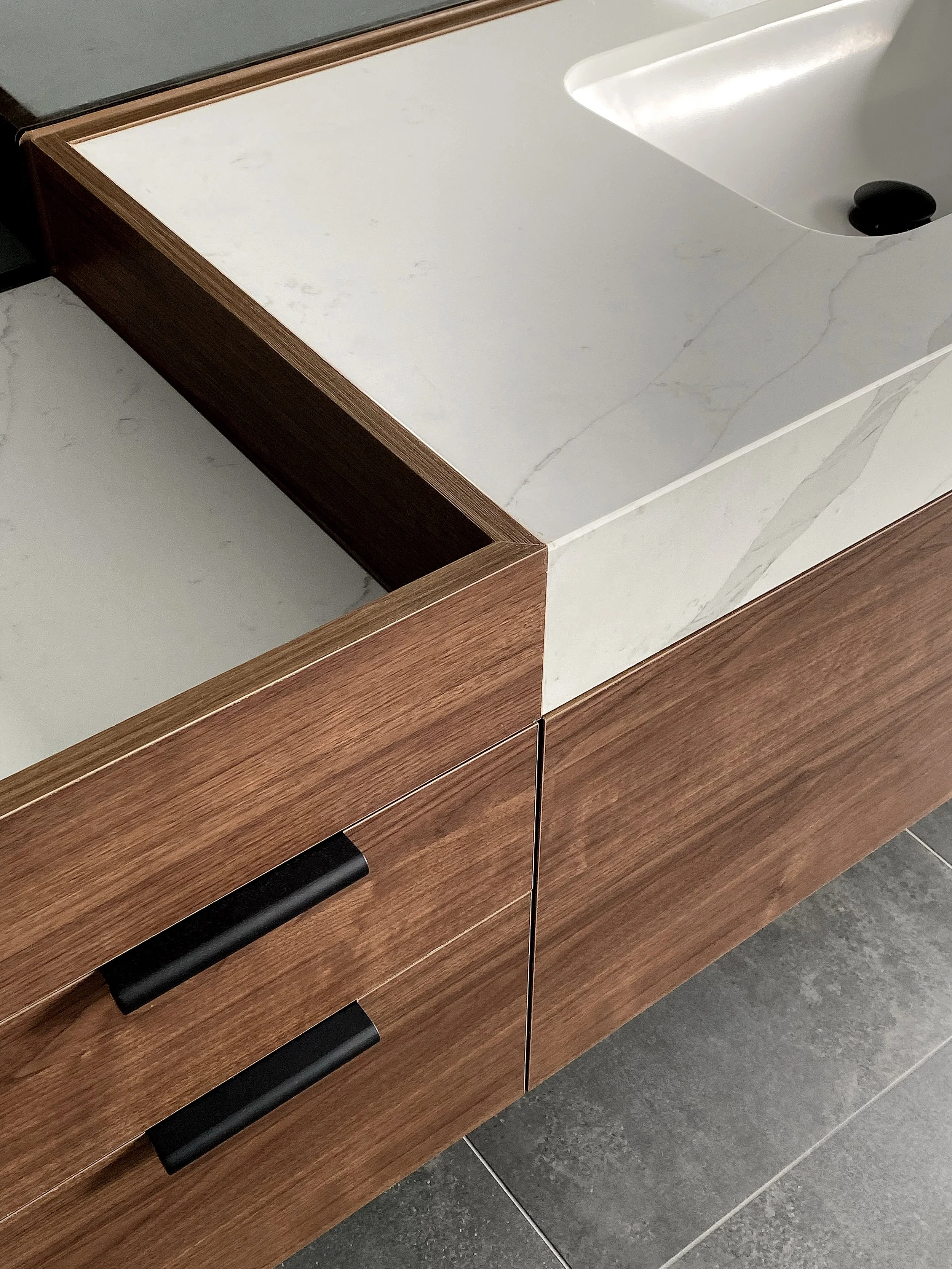 Close-up of timber vanity drawer with inset stone benchtop and black handles