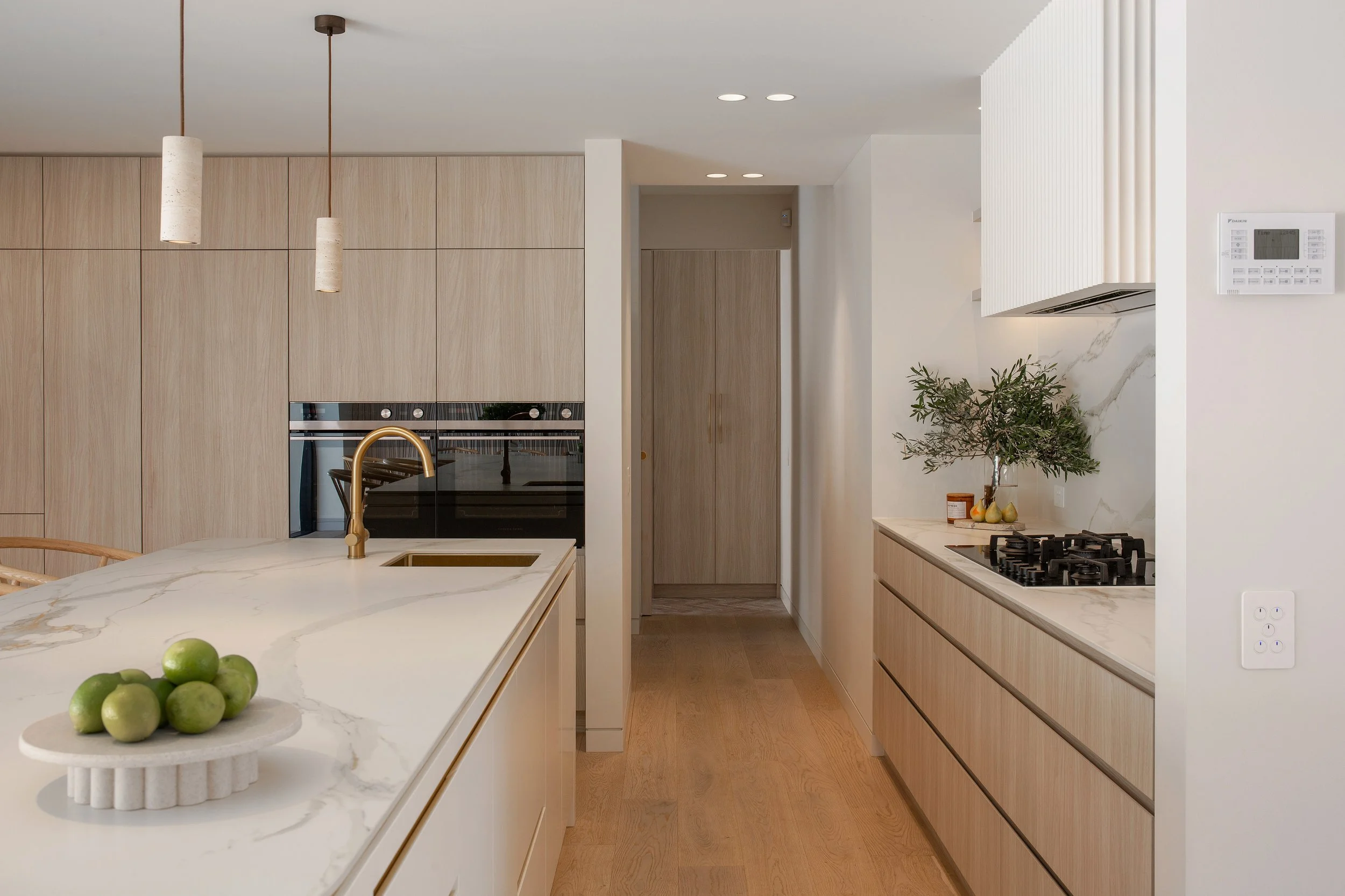 Kitchen at Dromana residence with timber cabinetry, marble benchtop, brass sink and integrated appliances