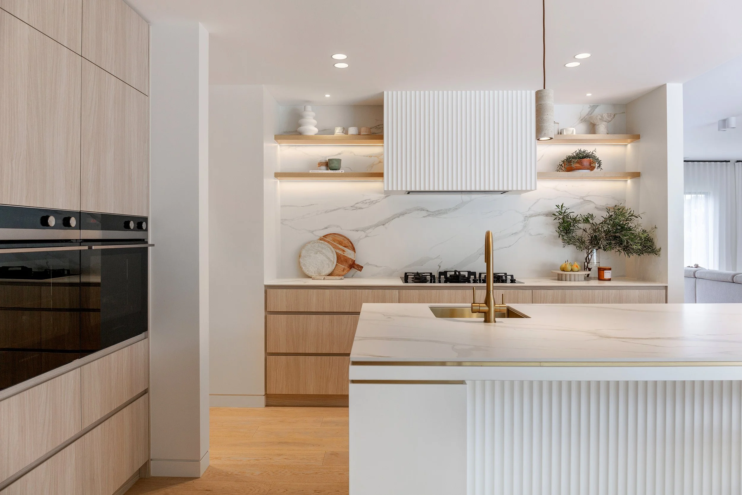 Kitchen at Dromana residence with marble island bench, brass tapware, timber cabinetry and fluted rangehood