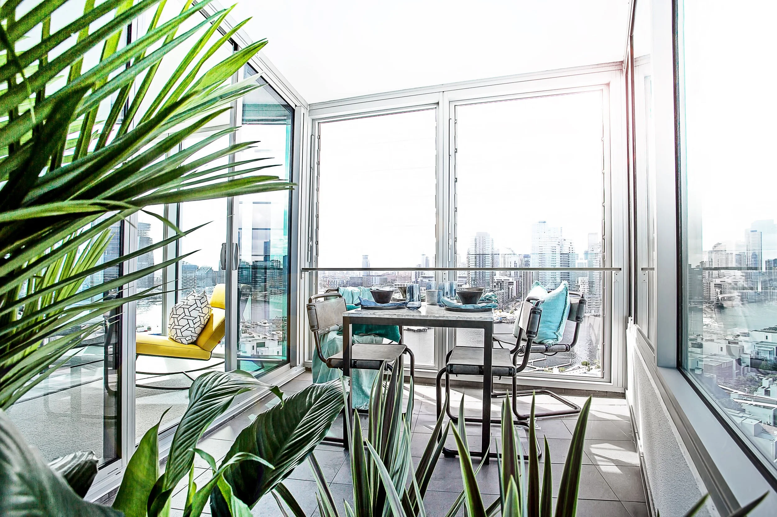 Winter garden dining area overlooking Yarra River with marble table, teal cushions and skyline views at Forge by Mirvac.