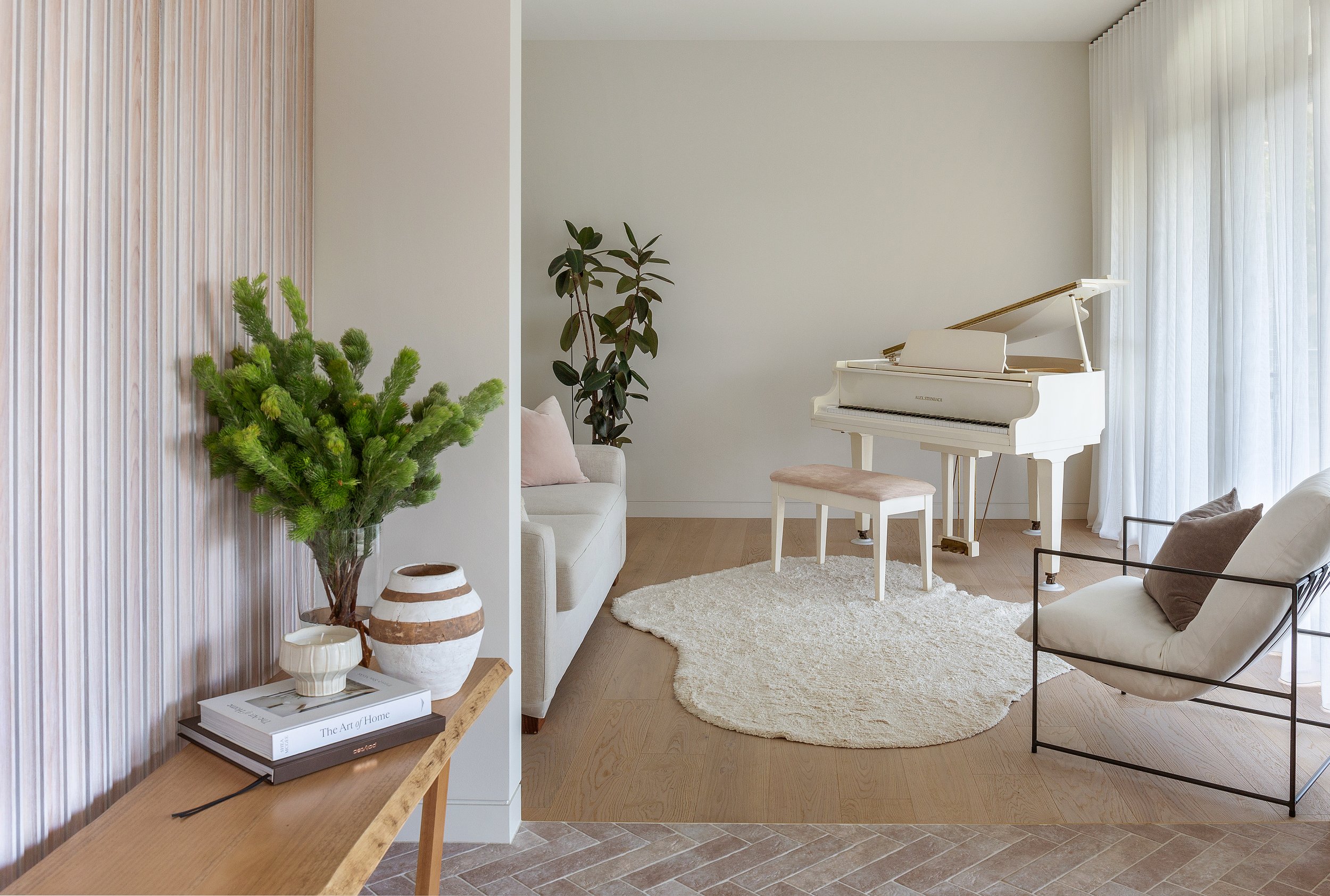 Music room at Dromana residence with white piano, soft neutral seating, timber floor and sheer curtain