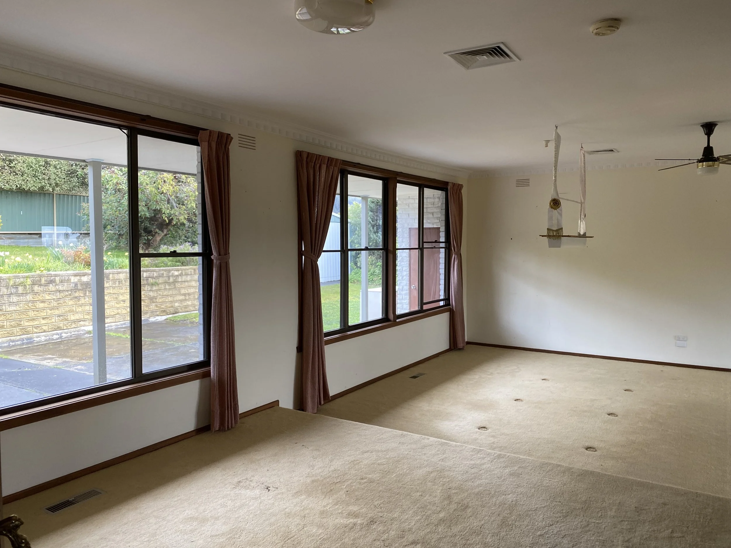 Dromana renovation before image of open living room with timber feature wall, arched doorway and original carpet