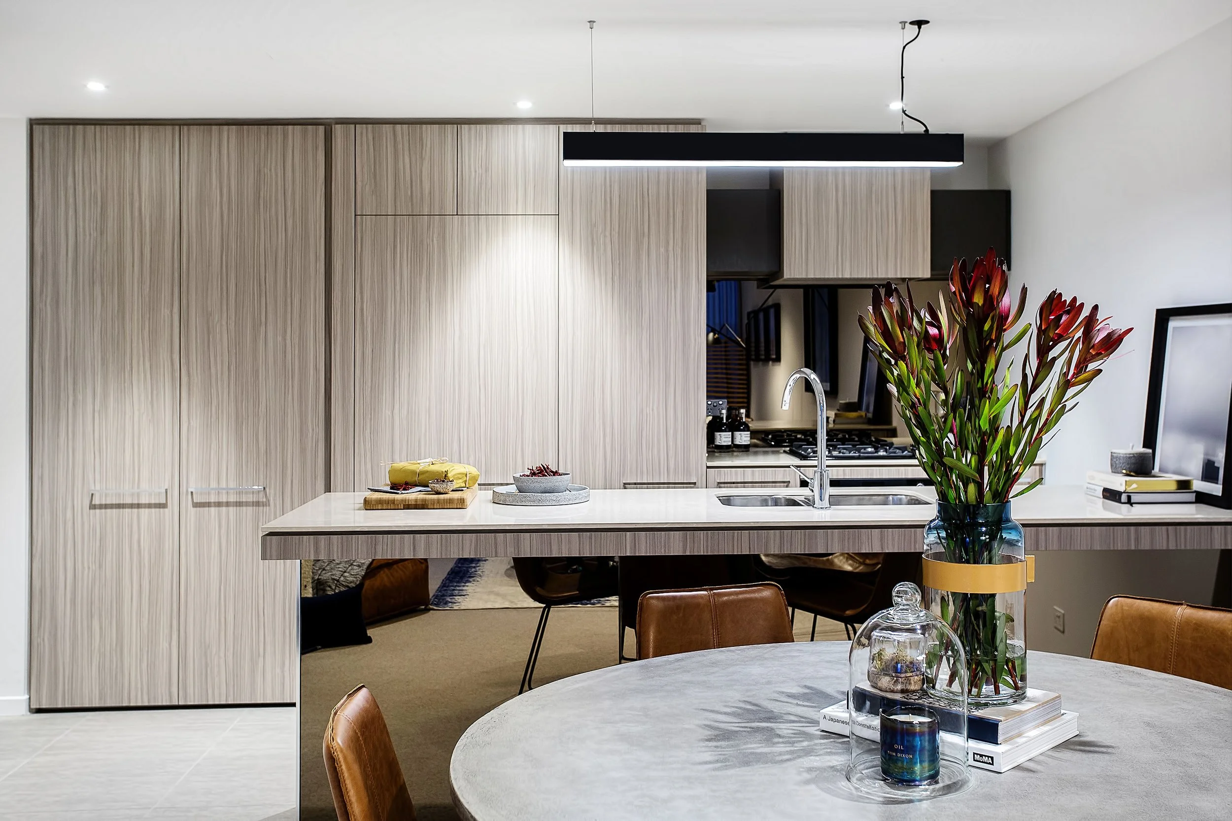 Kitchen island detail in Forge Docklands Apartment 204 with stone benchtop, chrome tapware and styled floral arrangement.