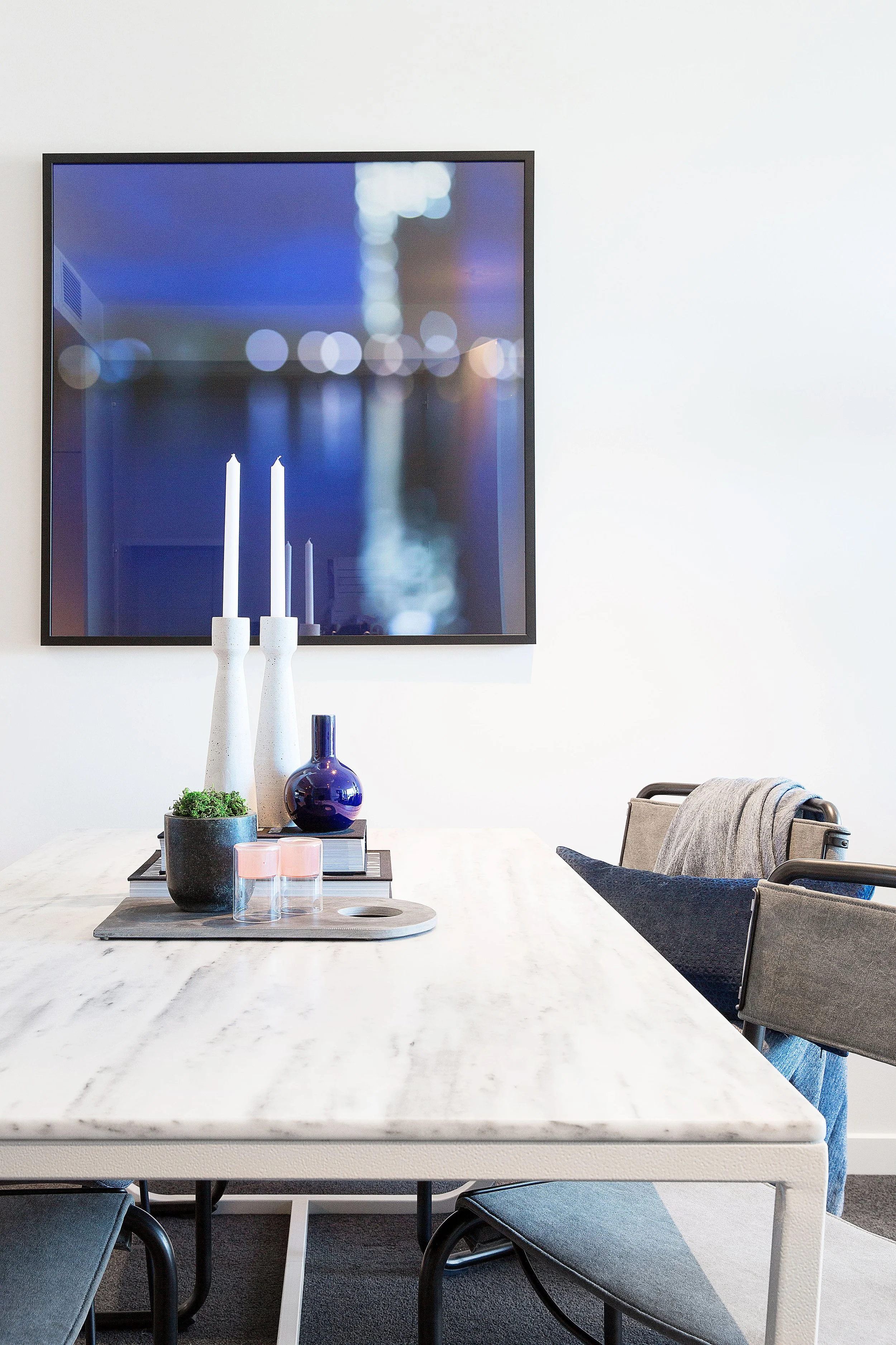 Contemporary dining setting with tray styling, blue glass and modern artwork backdrop in Melbourne loft apartment display suite.
