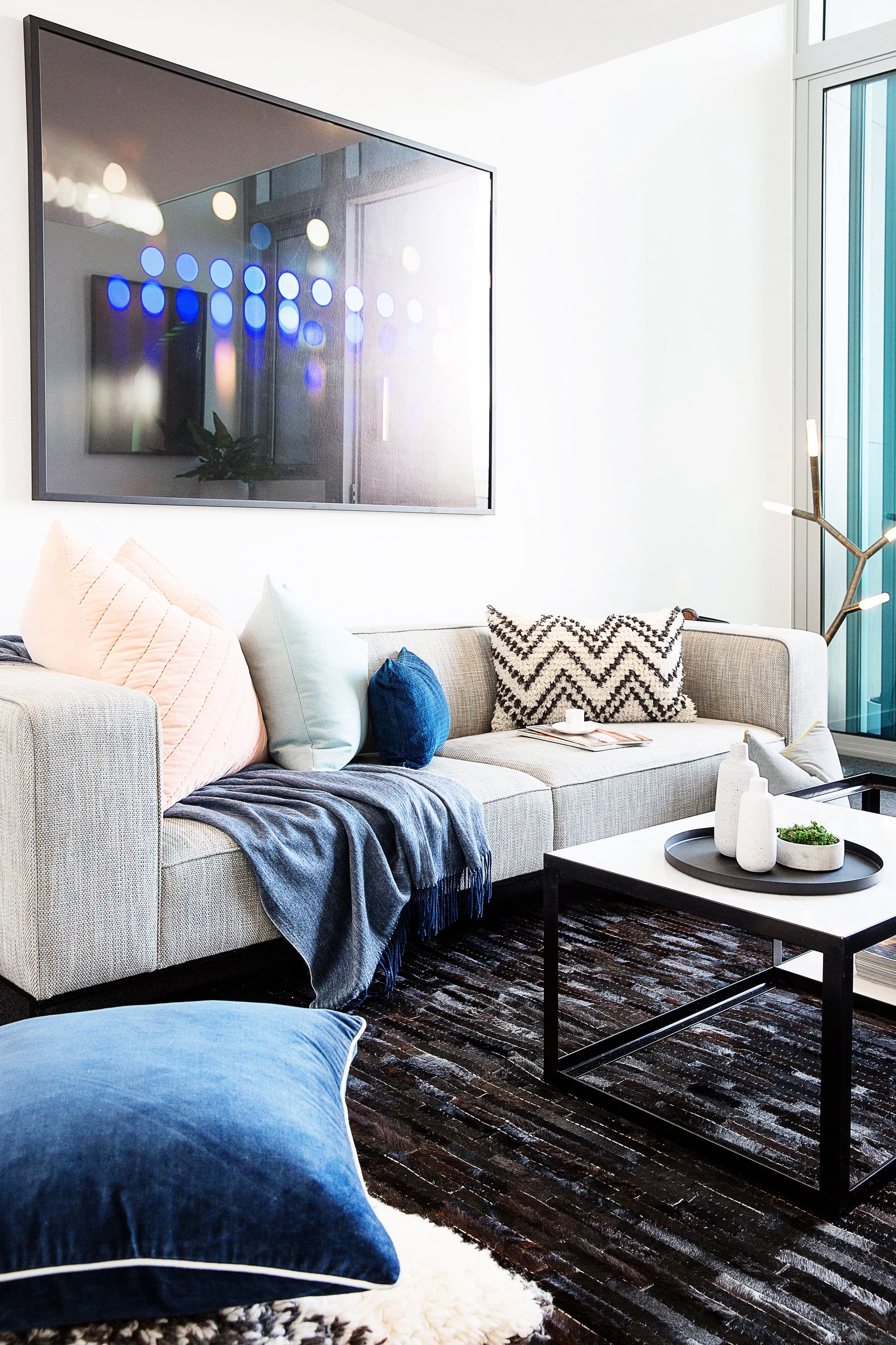 Neutral sofa layered with graphic cushions and deep blue accents, creating a refined New York inspired loft aesthetic. Interior styling by DMP Creative, Melbourne.