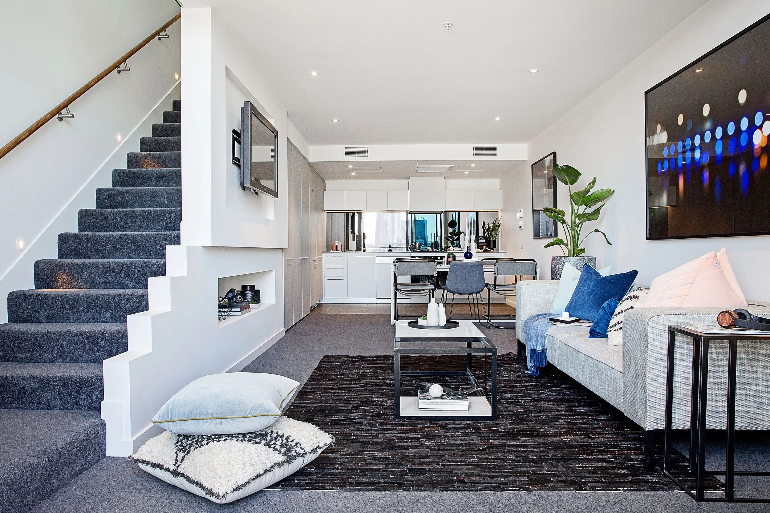 Double-height loft apartment featuring open plan living, staircase detail and contemporary kitchen beyond. Styled to highlight spatial flow and modern urban living at Forge, Yarra’s Edge.