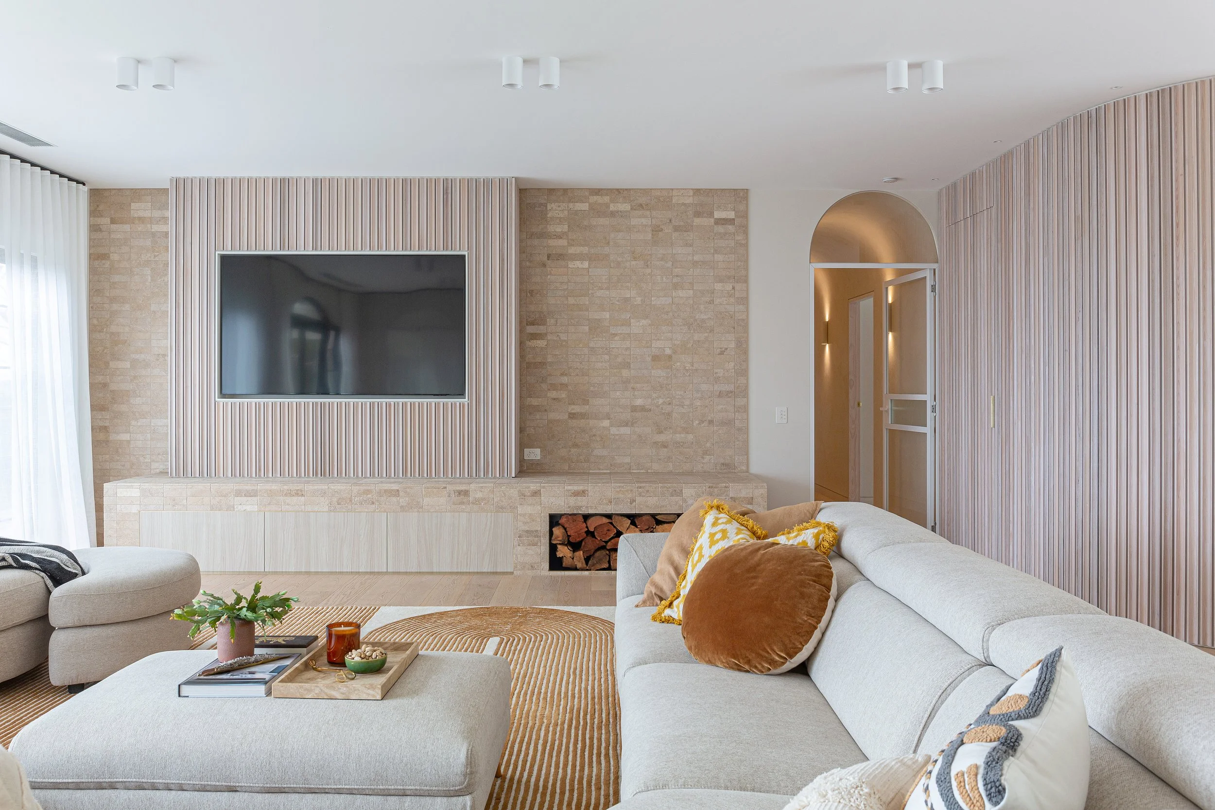 Living room at Dromana residence with arched black-framed windows, neutral seating and fluted timber TV wall