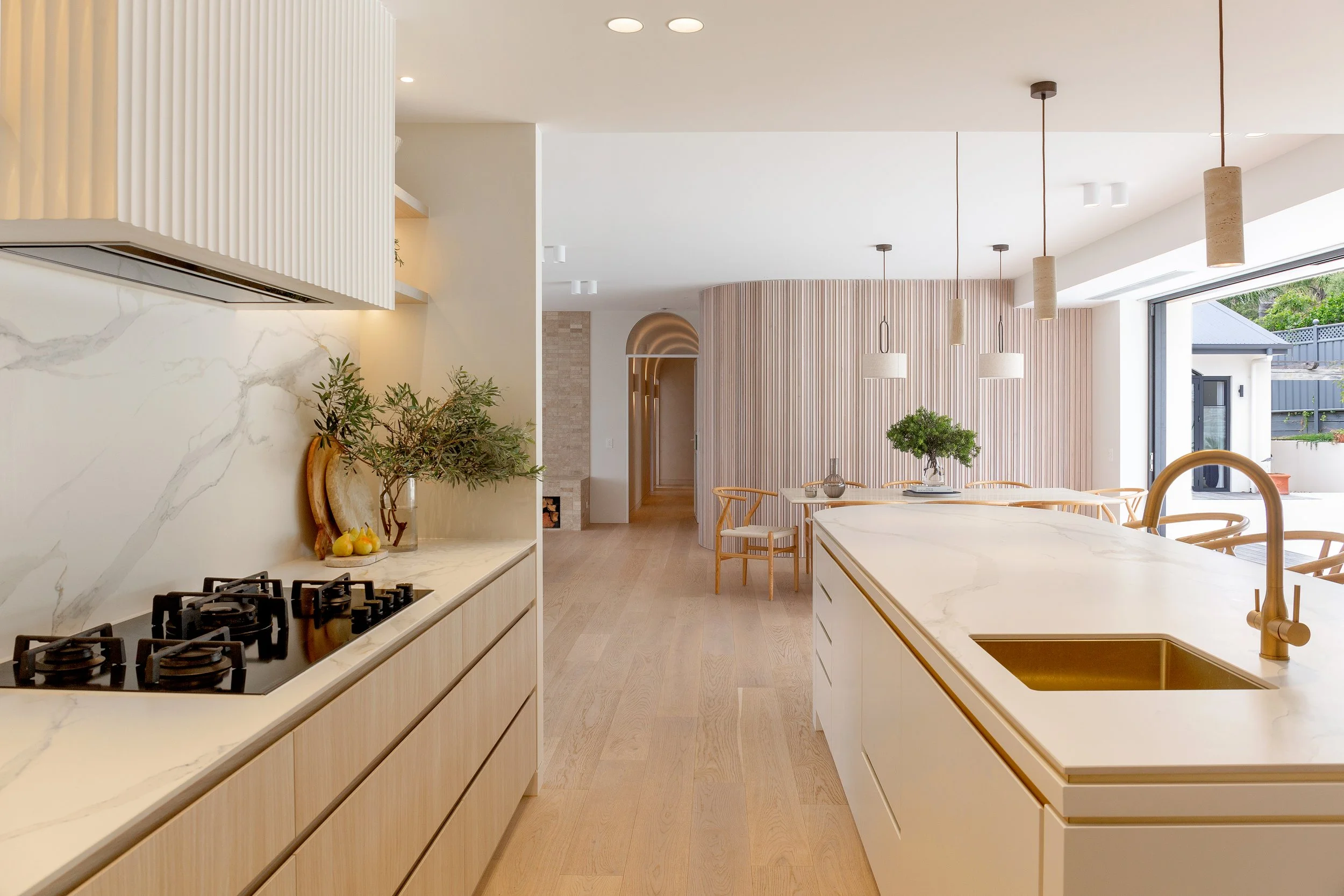 Open plan kitchen at Dromana residence with marble island, brass sink, pendant lights and view to dining area