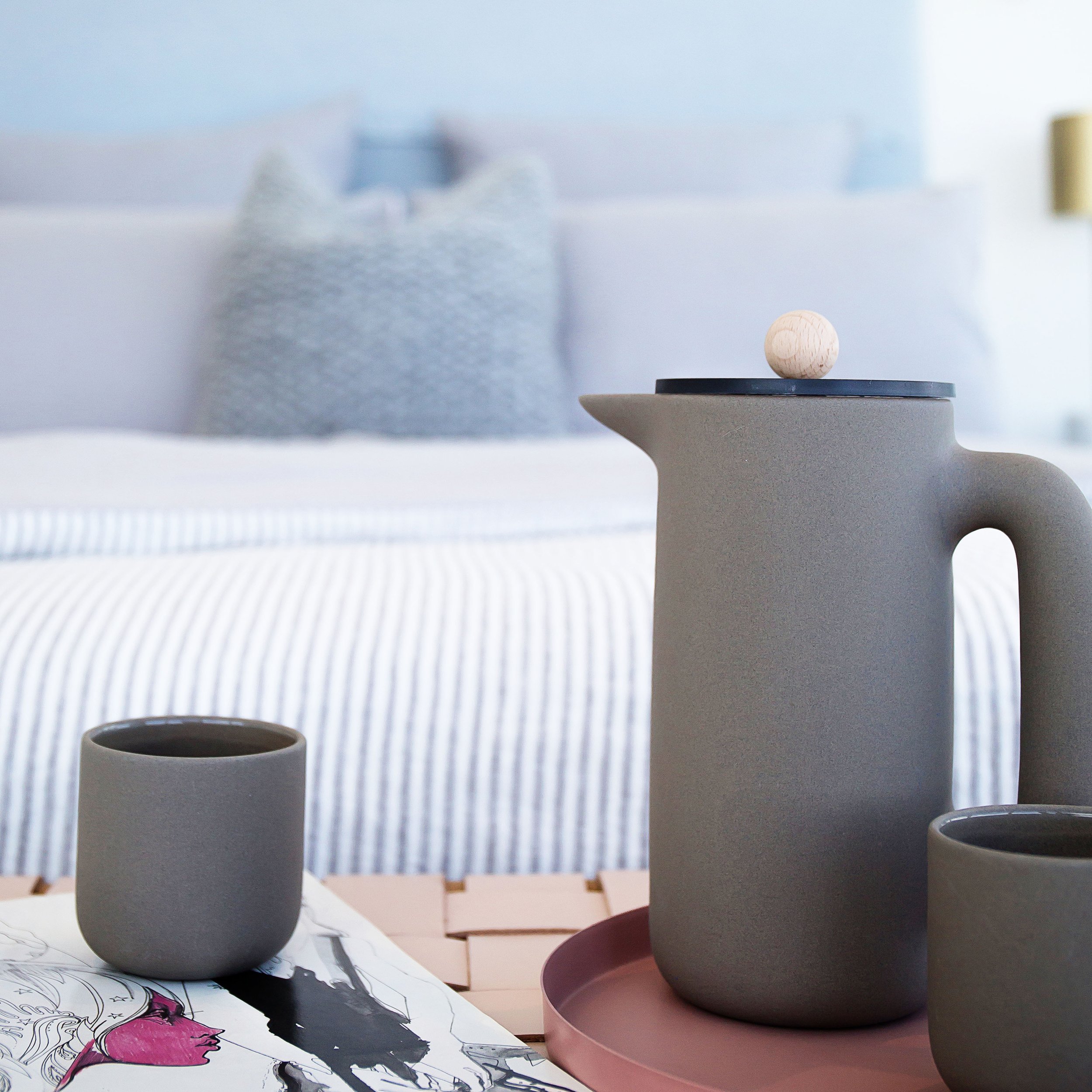 Bedroom styling detail with ceramic carafe and cups on woven bench, showcasing layered textiles in Mirvac Forge display apartment.