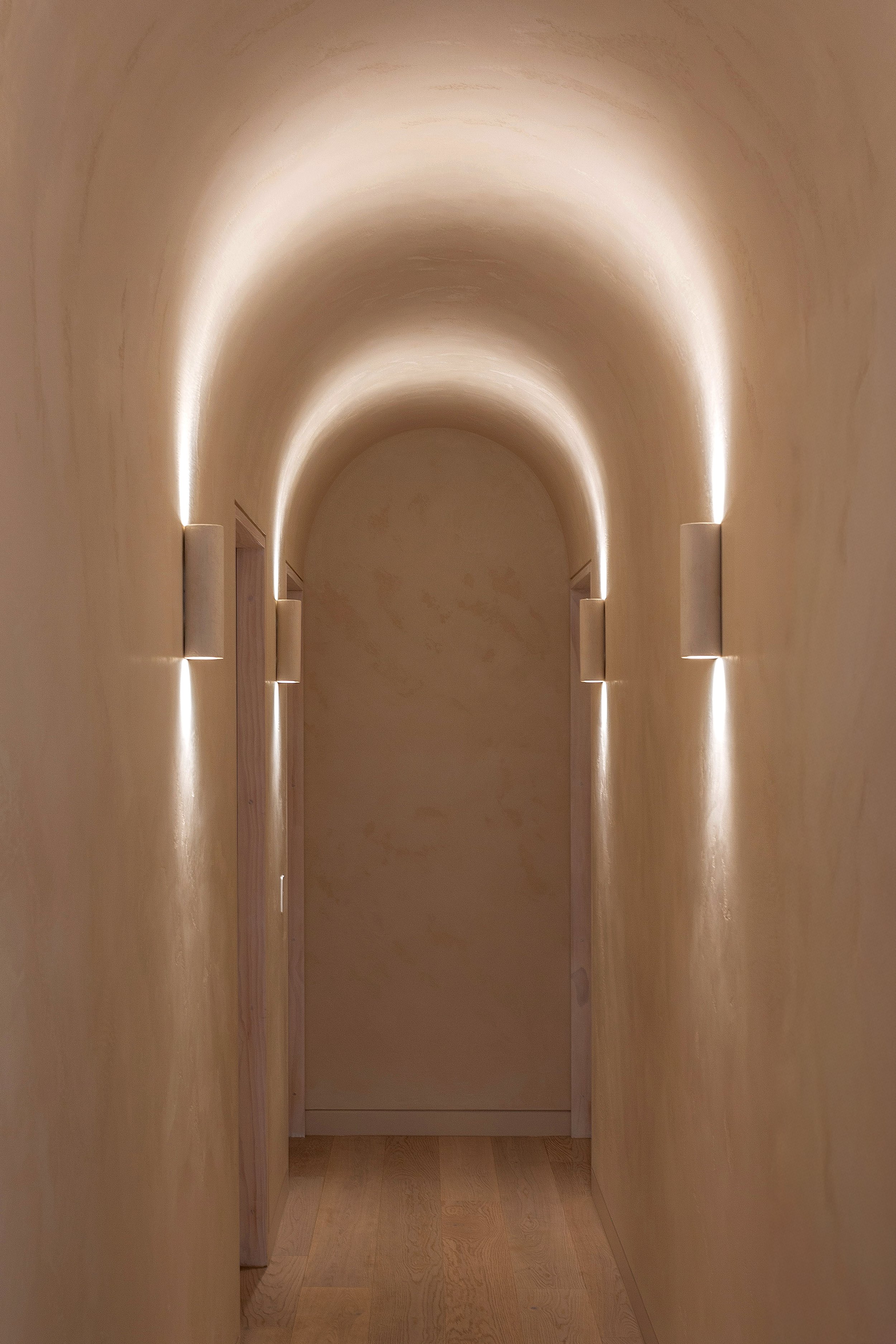 Arched hallway at Dromana residence with soft integrated wall lighting and warm venetian plaster finish
