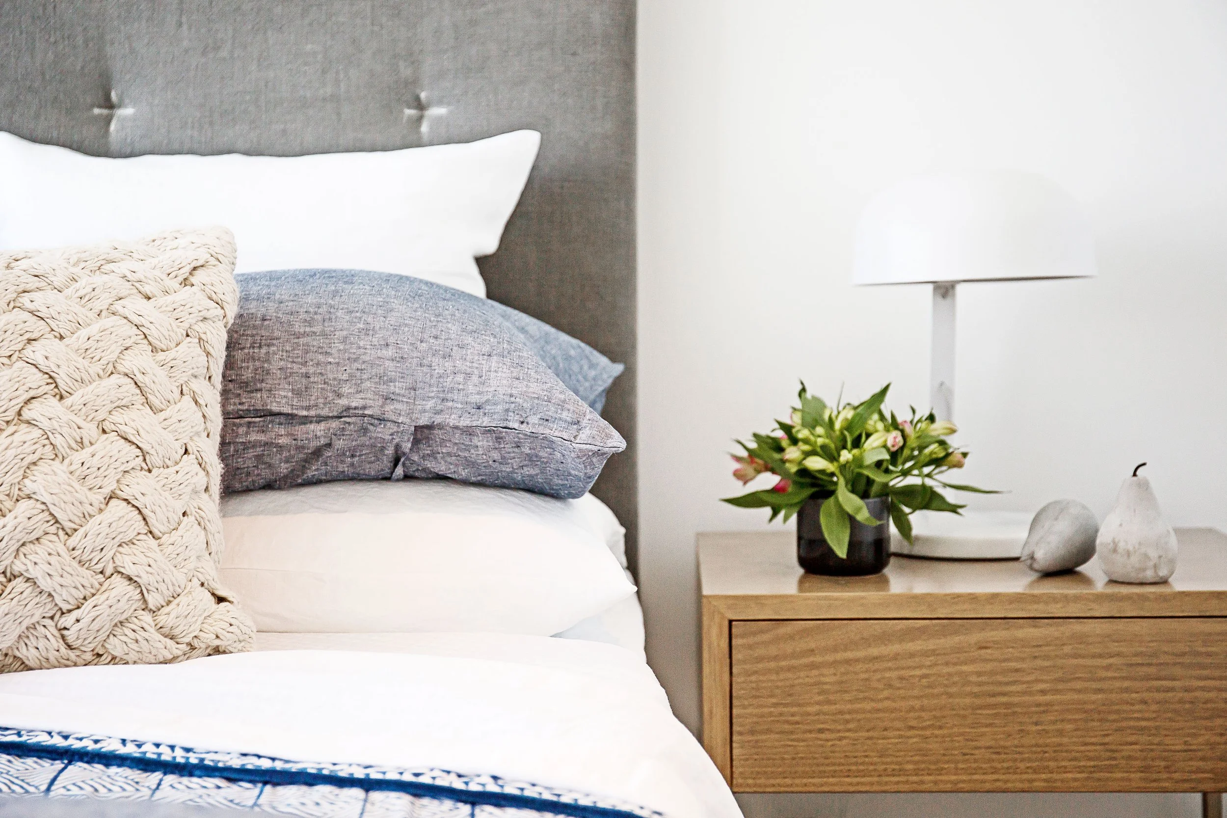 Bedroom bedside styling detail with textured cushions, table lamp and greenery in Mirvac Forge apartment.