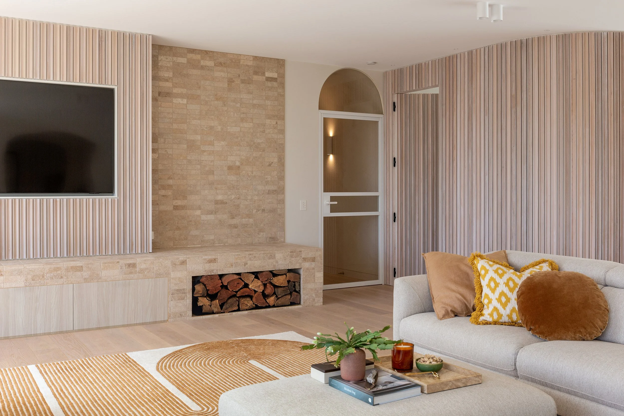 Living room at Dromana residence with stone fireplace, fluted timber cabinetry, neutral sofa and textured rug