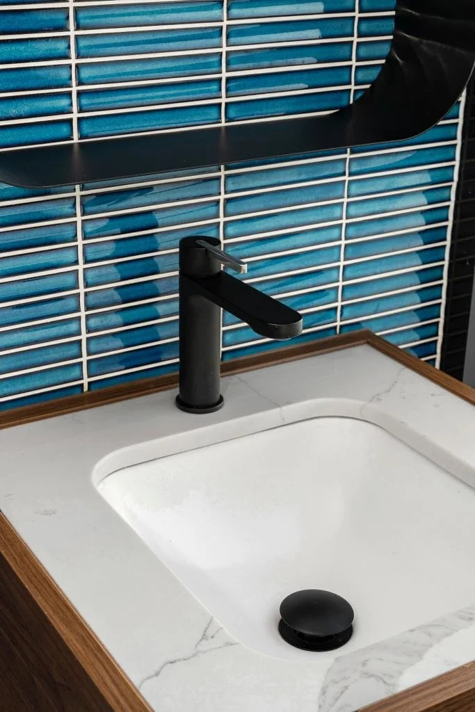 Close-up of bathroom basin with blue tile splashback and black tapware