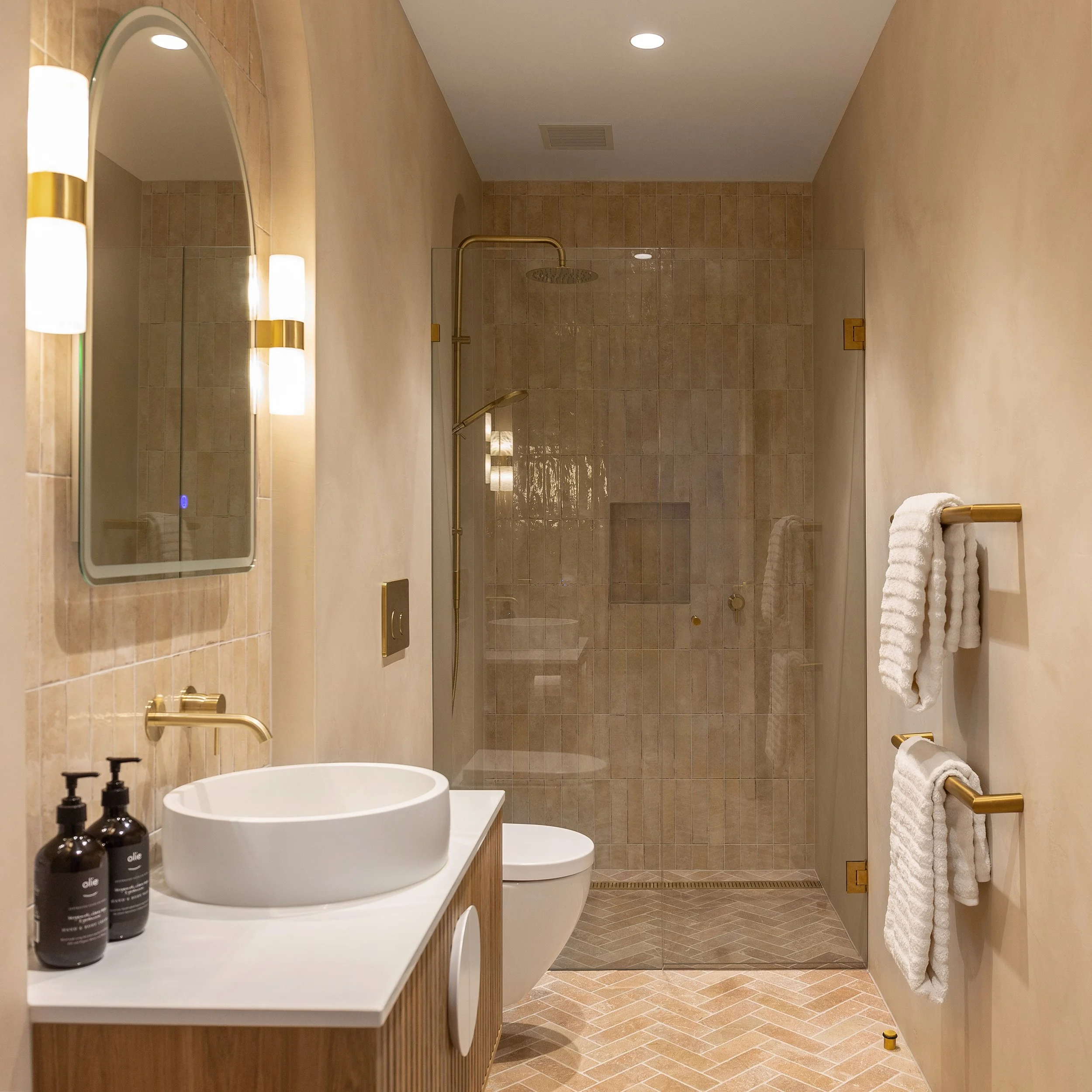 Bathroom at Dromana residence with neutral tiles, brass shower fittings, timber vanity and herringbone floor tiles
