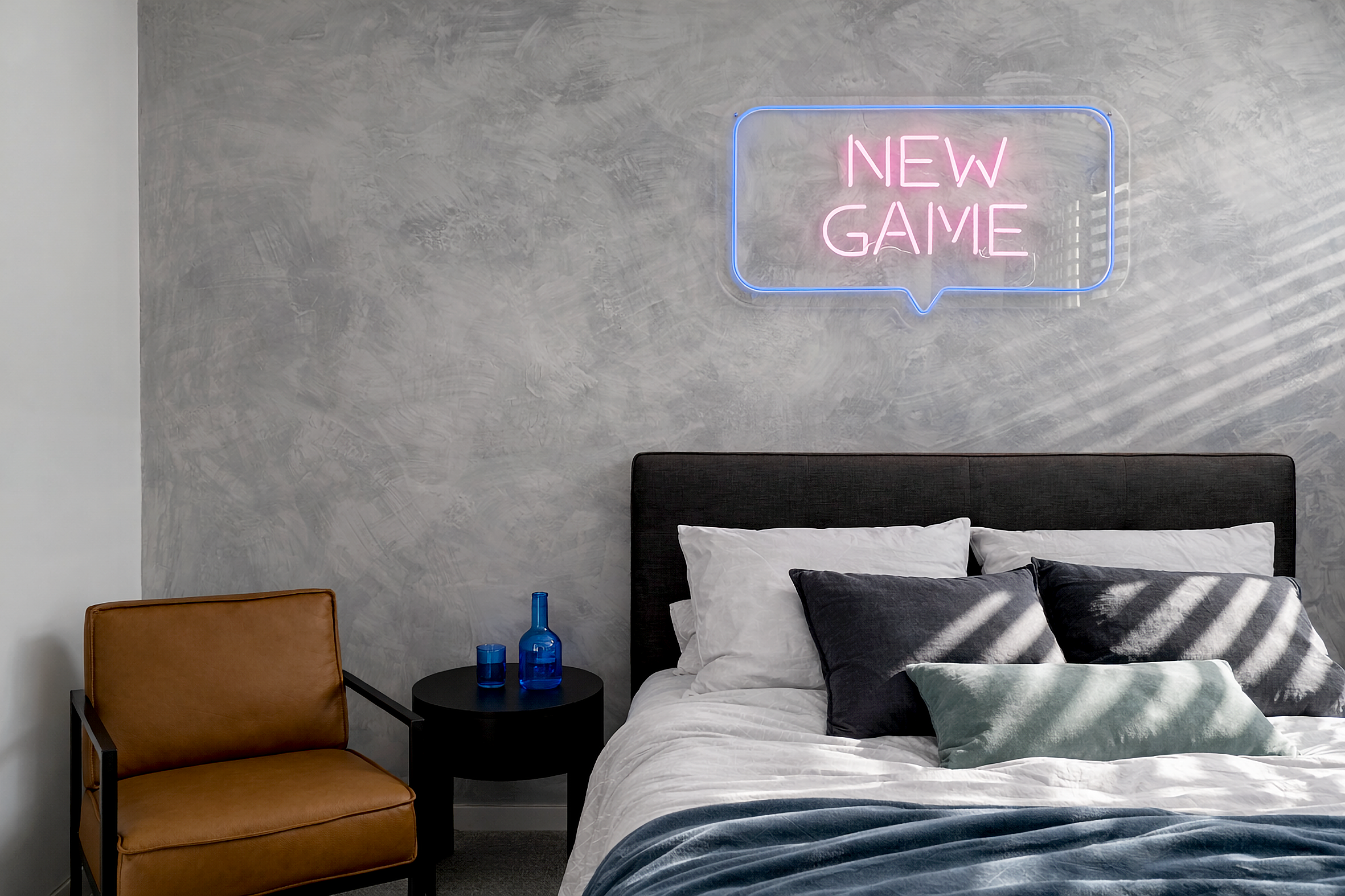 Bedroom with textured grey wall and neon artwork above bed