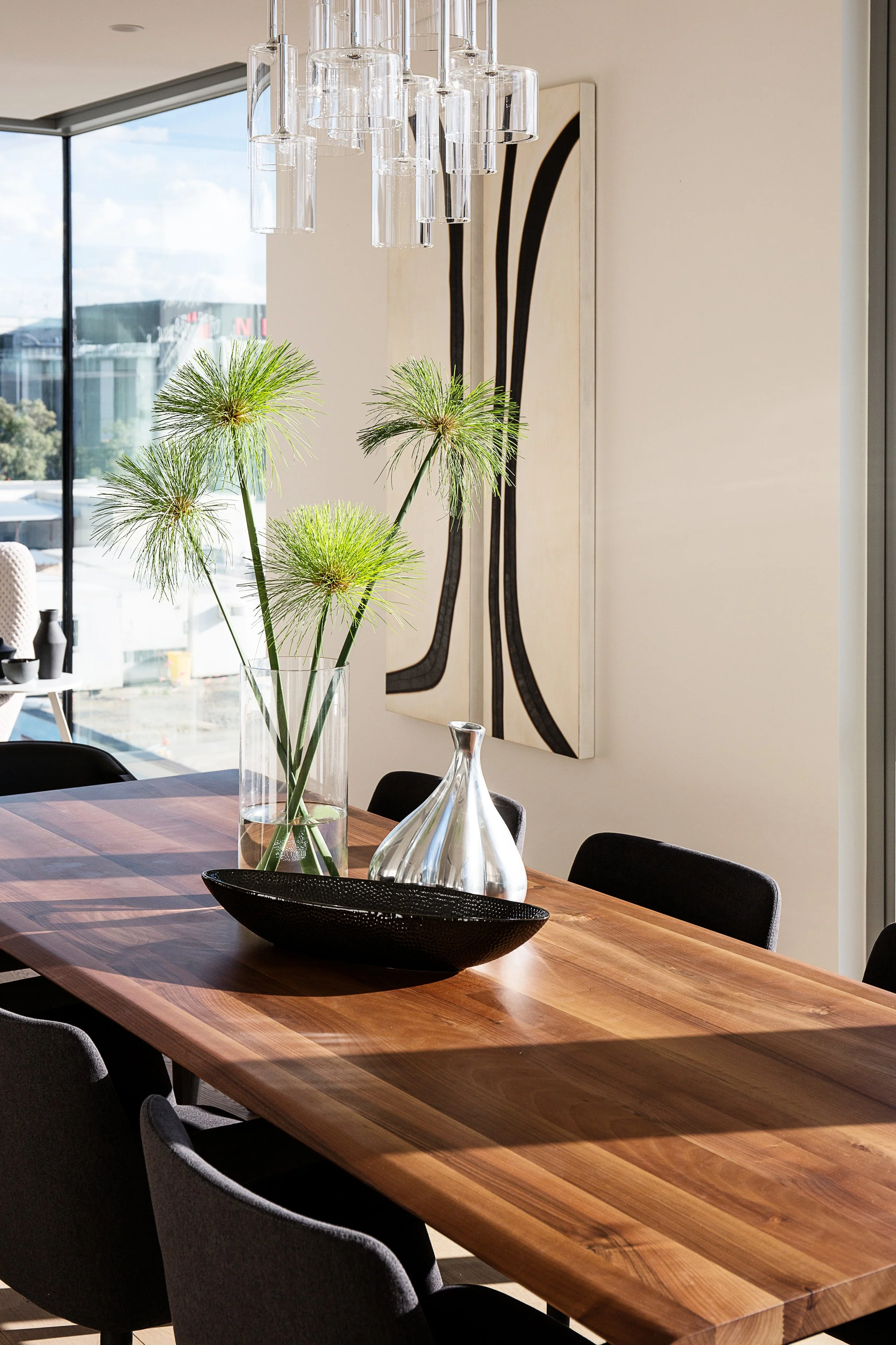Modern dining room with solid timber dining table, black upholstered dining chairs, sculptural glass pendant lighting and minimal styling, overlooking city views in a luxury Docklands apartment.
