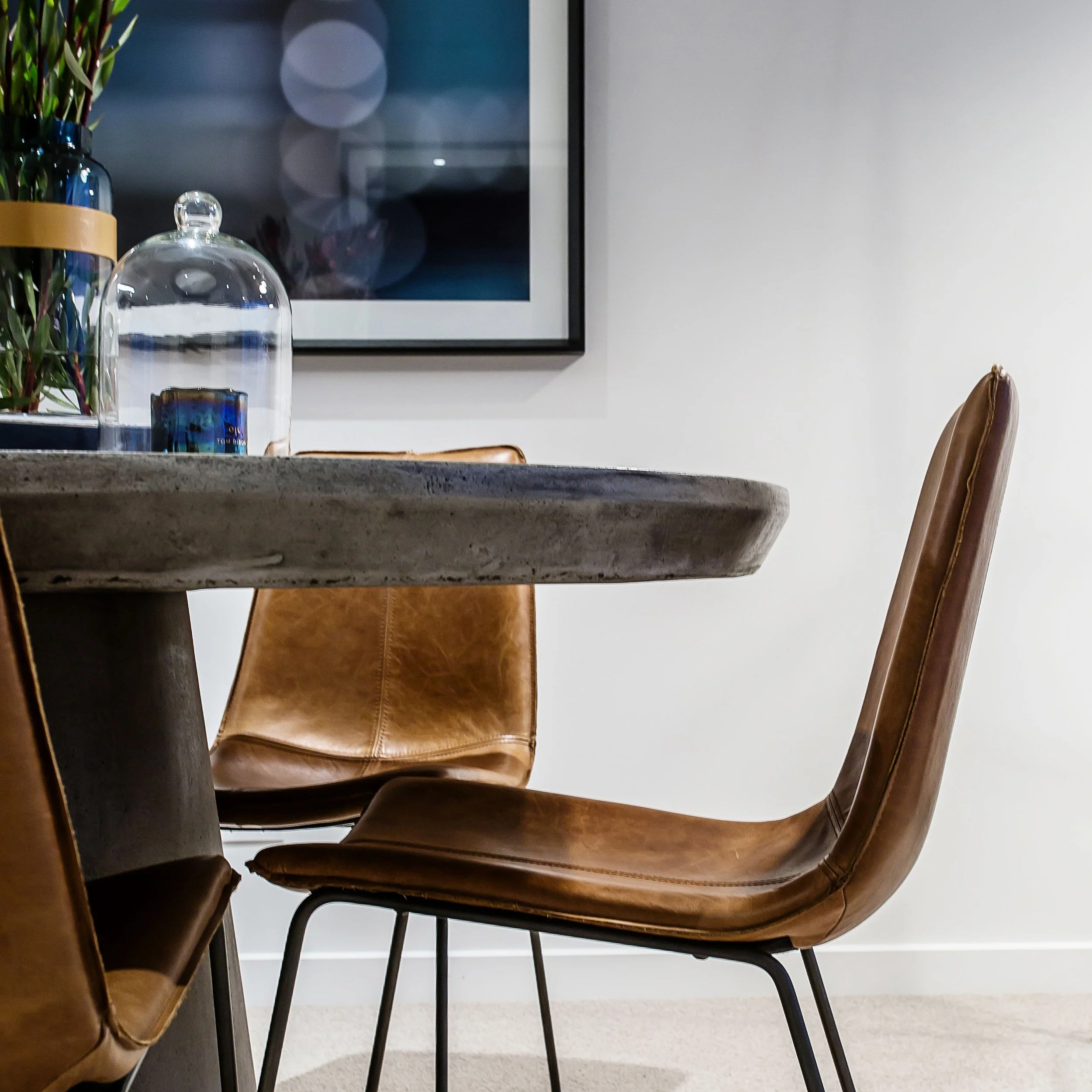 Concrete round dining table with tan leather chairs in Apartment 204 at Forge Docklands, styled with glass cloche and floral arrangement.