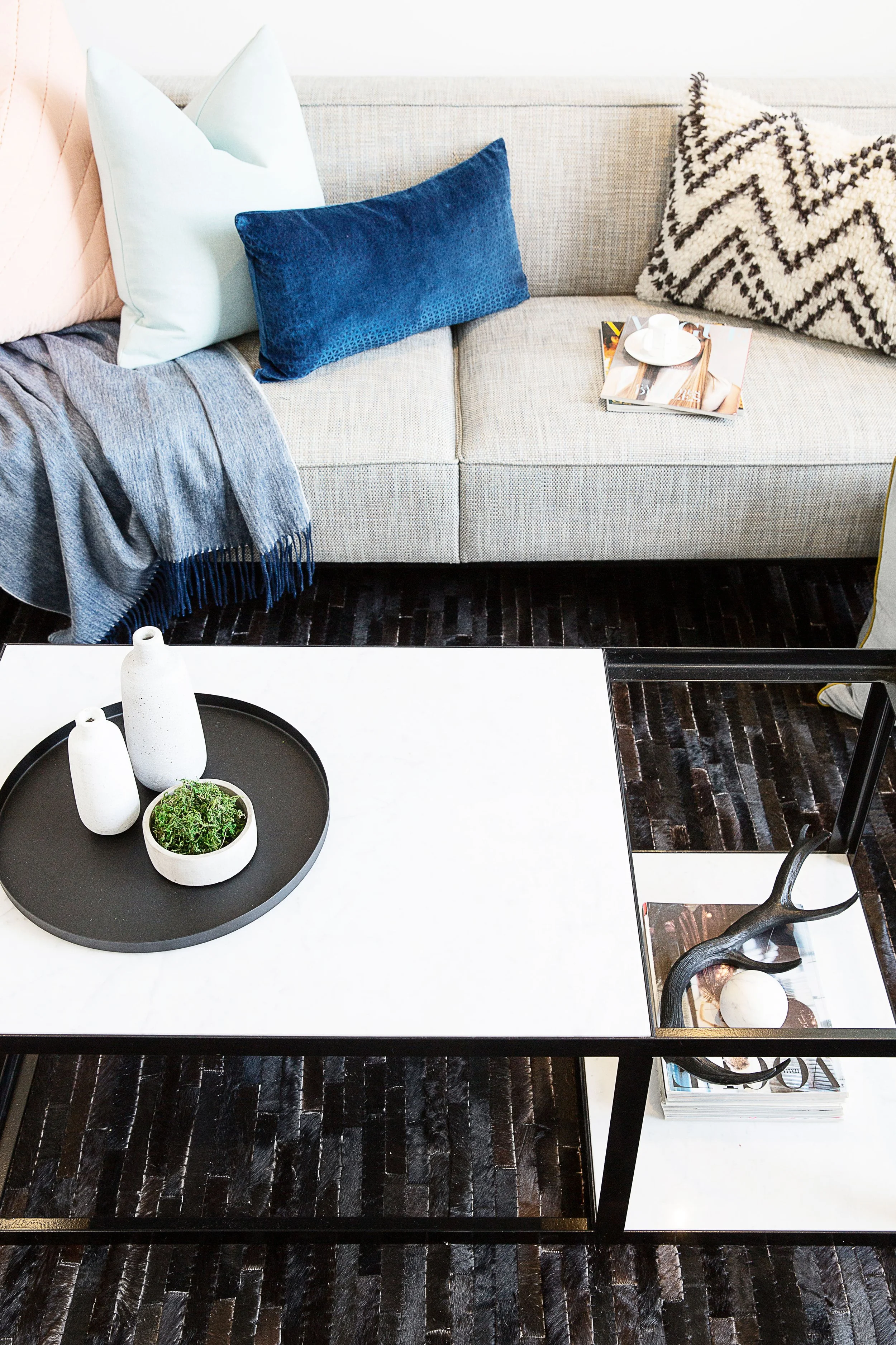 Minimal coffee table styling with ceramic vessels and greenery, set against textured rug and modern sofa in a Forge loft apartment display suite.