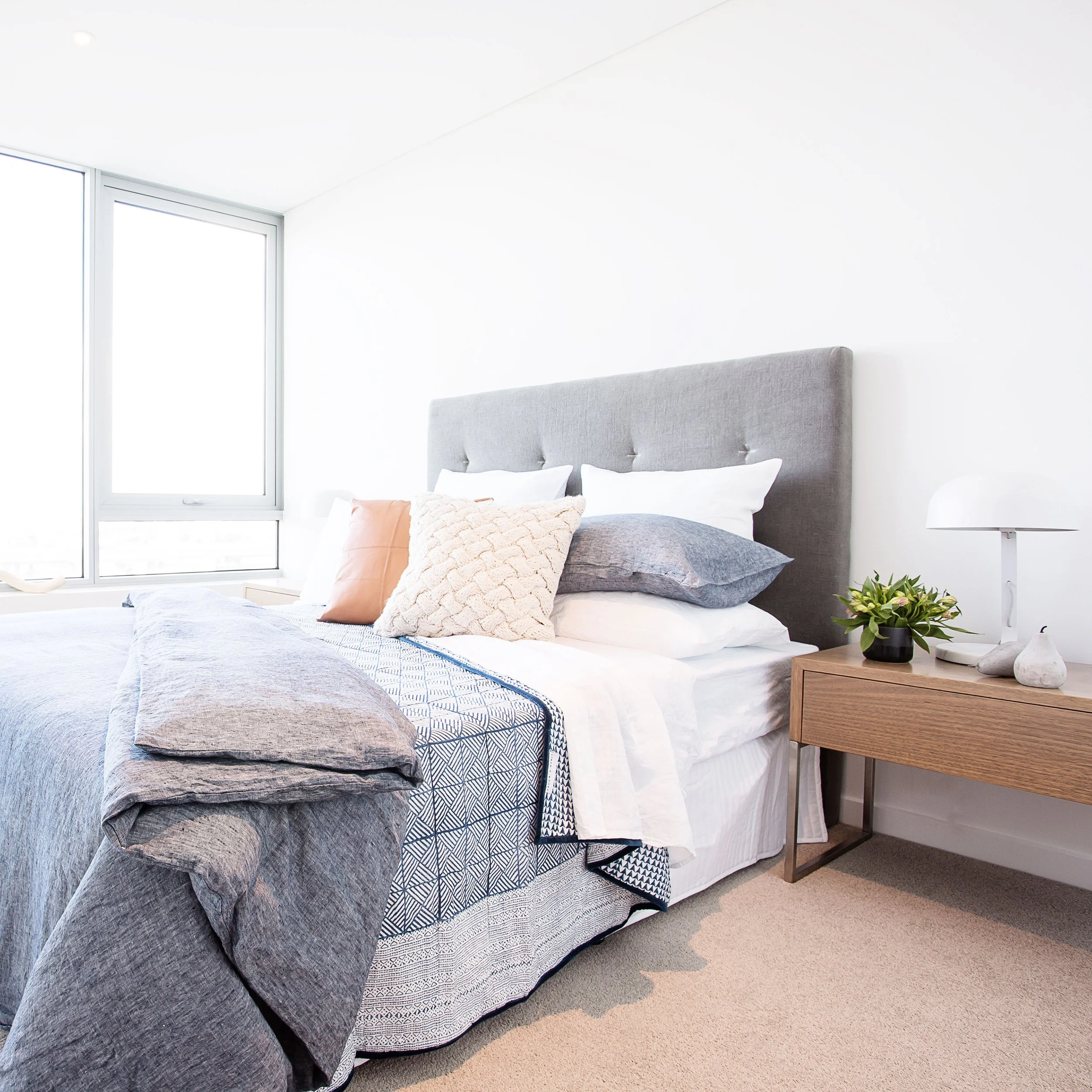 Two bedroom display apartment bedroom at Forge Docklands styled with layered linen bedding and timber bedside table.