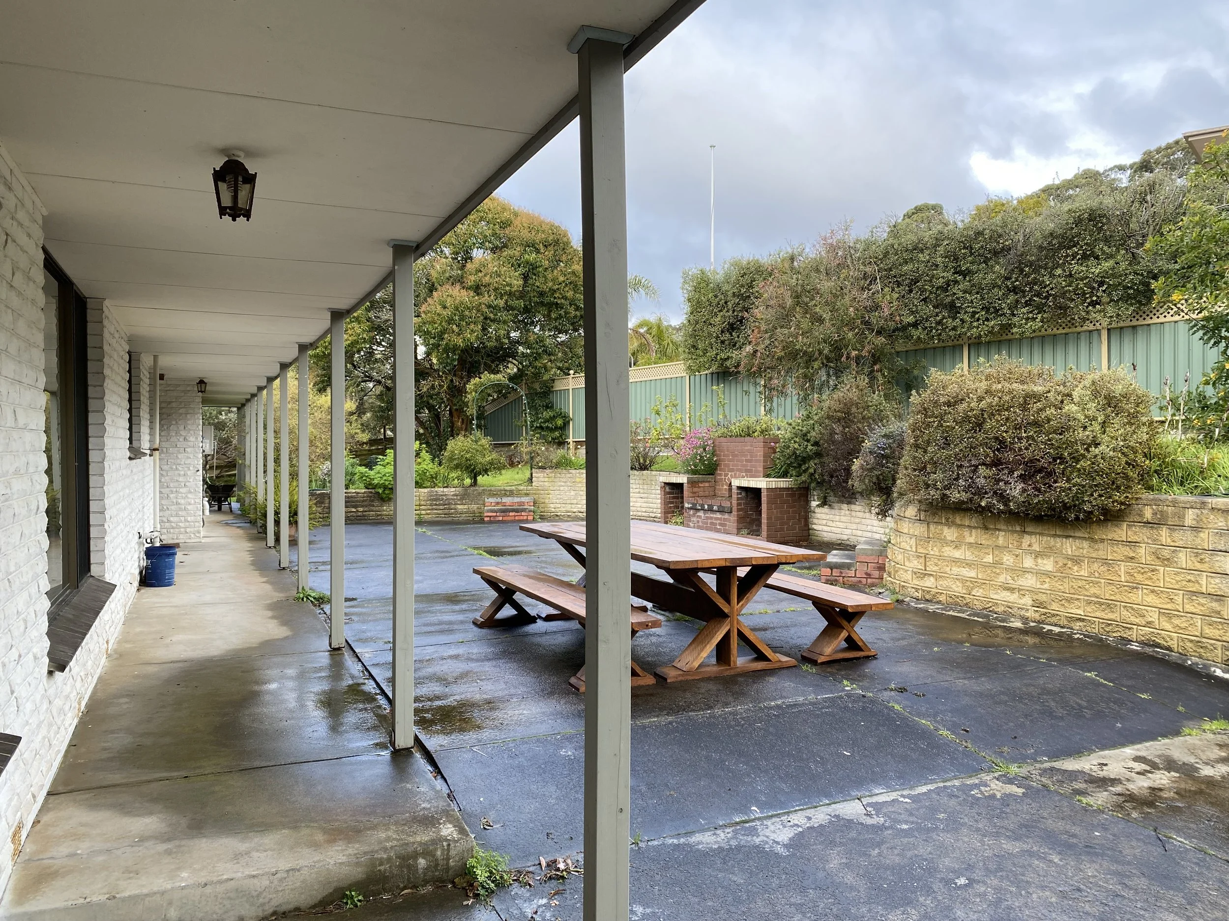 Dromana renovation before image of rear exterior with concreted outdoor area, garden beds and original brick facade