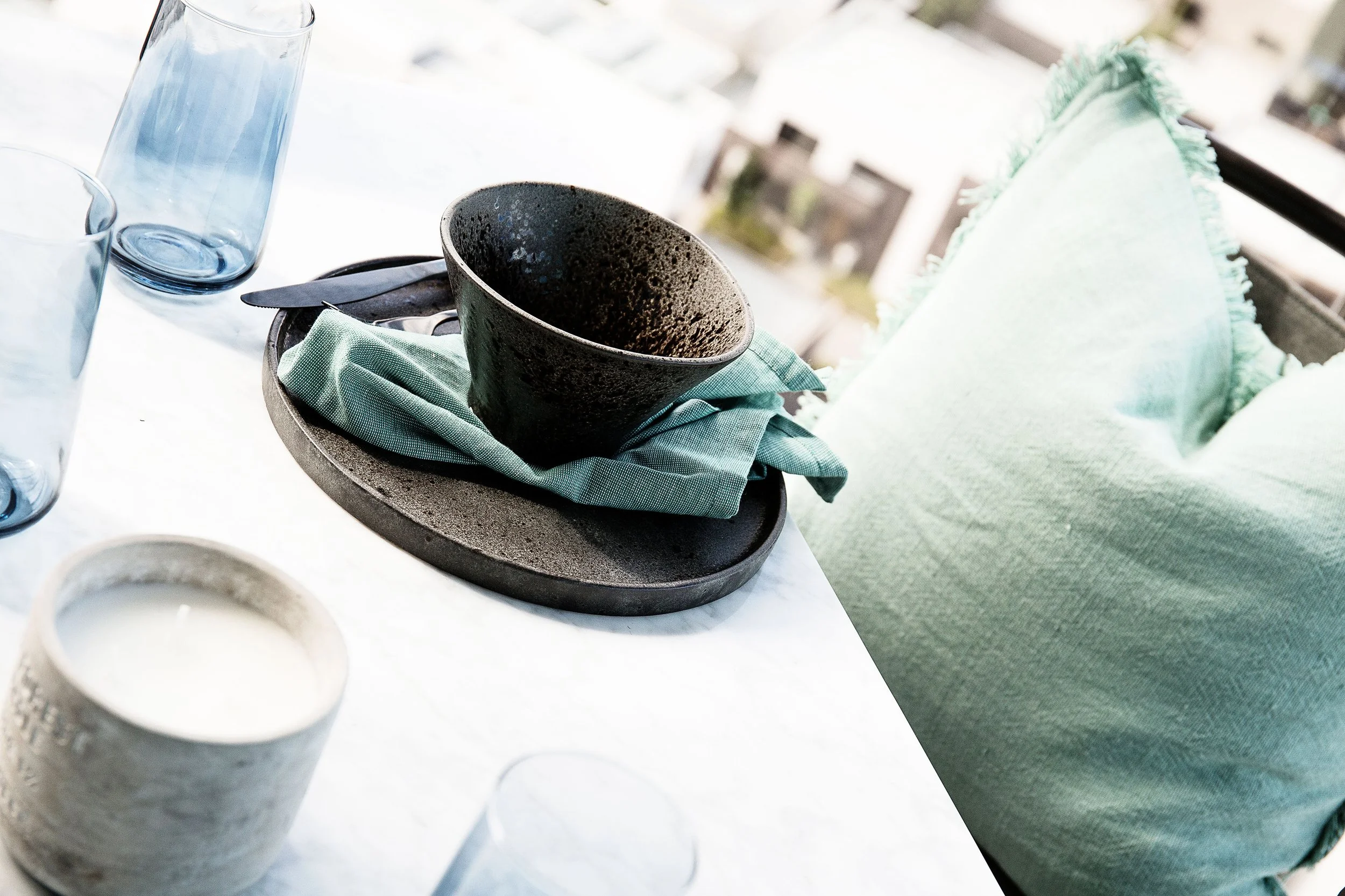 Black ceramic bowl and plate styled with a teal linen napkin on a marble table in a winter garden at Forge Yarra’s Edge, Apartment 1506, Melbourne.