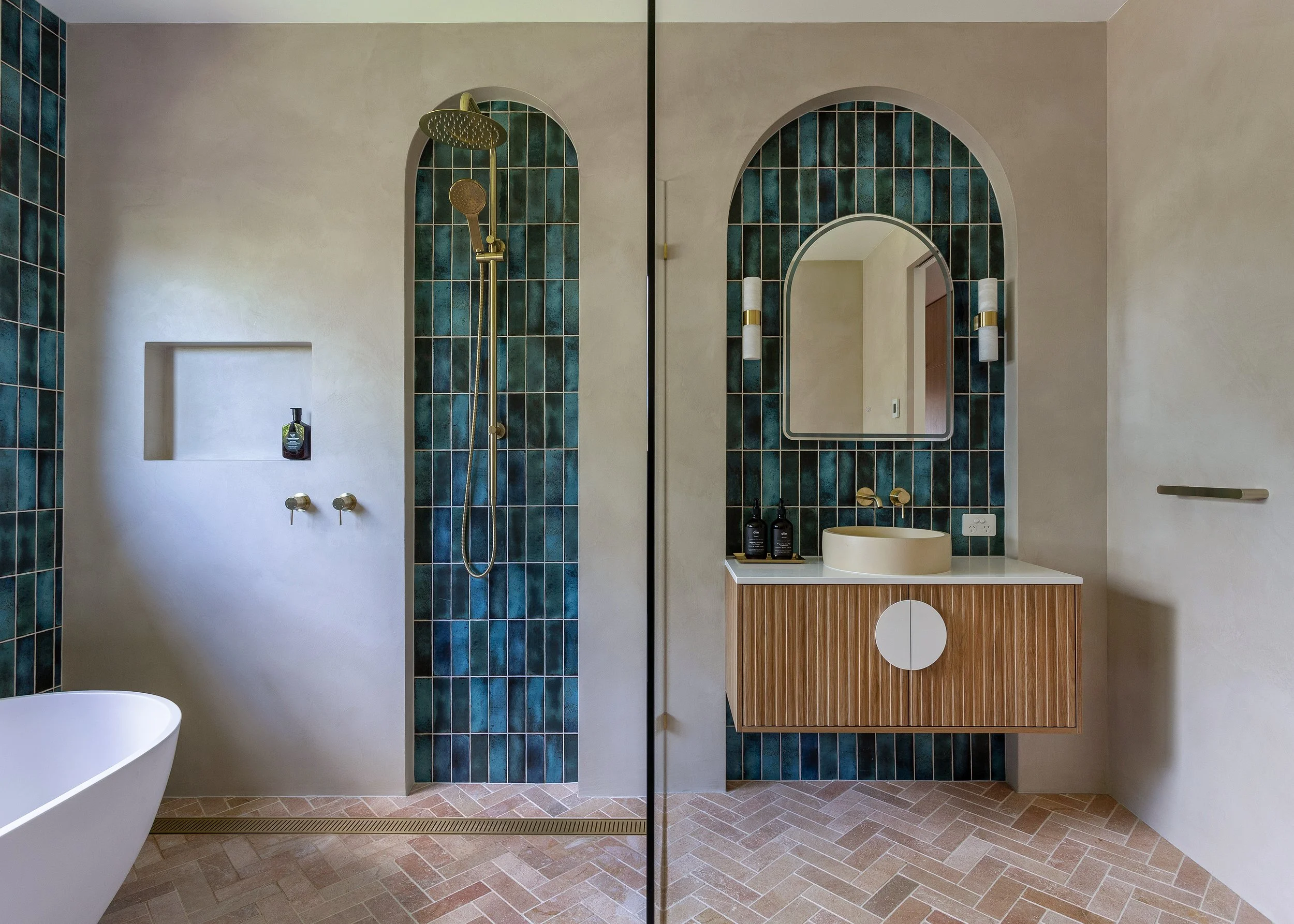 Bathroom at Dromana residence with green tiled arches, freestanding bath, fluted timber vanity and brass fixtures