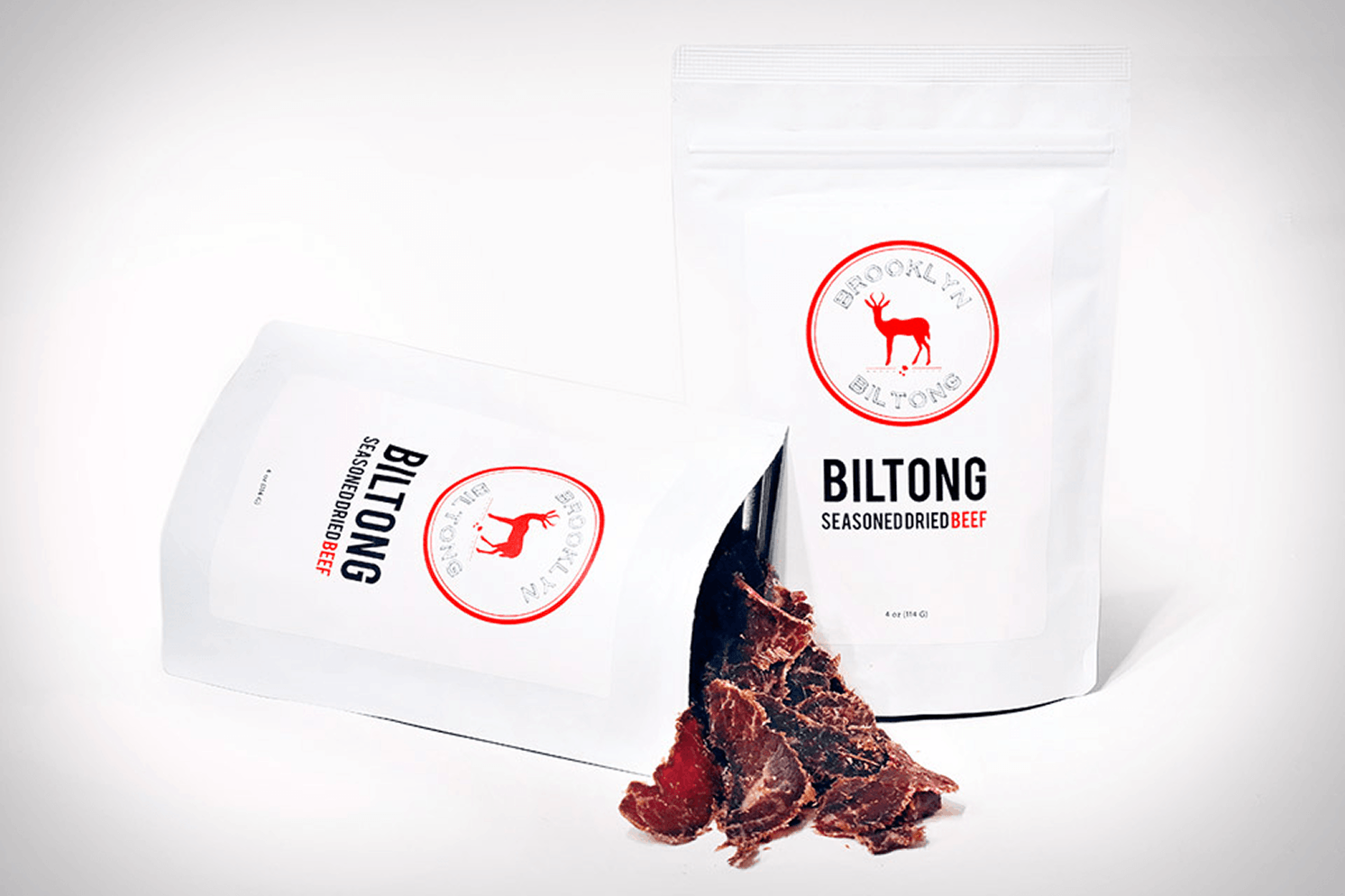Two early Brooklyn Biltong white packaging designs with red antelope logos, displayed alongside slices of dried beef.