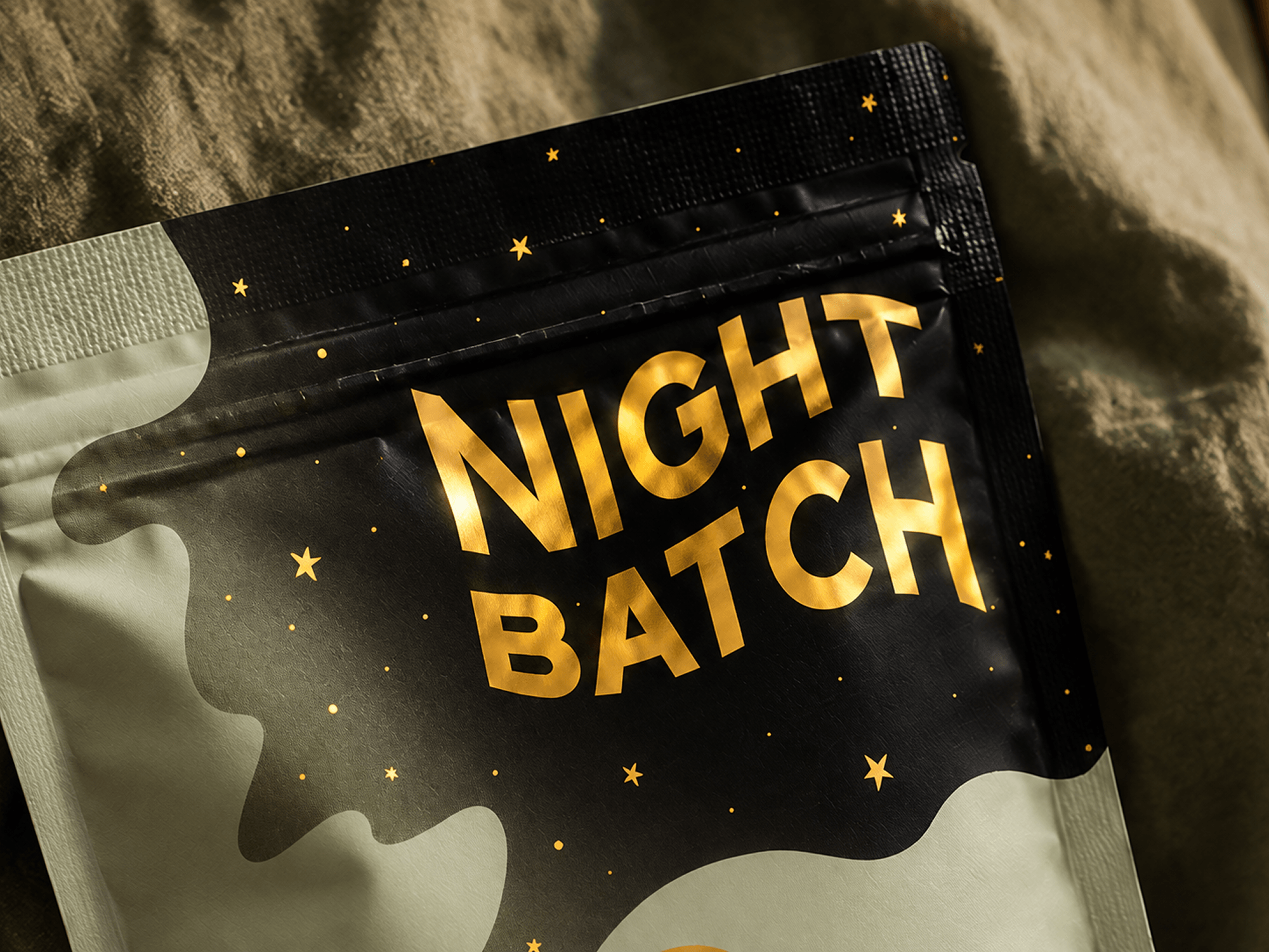 Close-up of Nightbatch packaging showing metallic gold typography, scattered stars, and a layered black night sky transitioning into a pale green pouch to demonstrate print opacity.