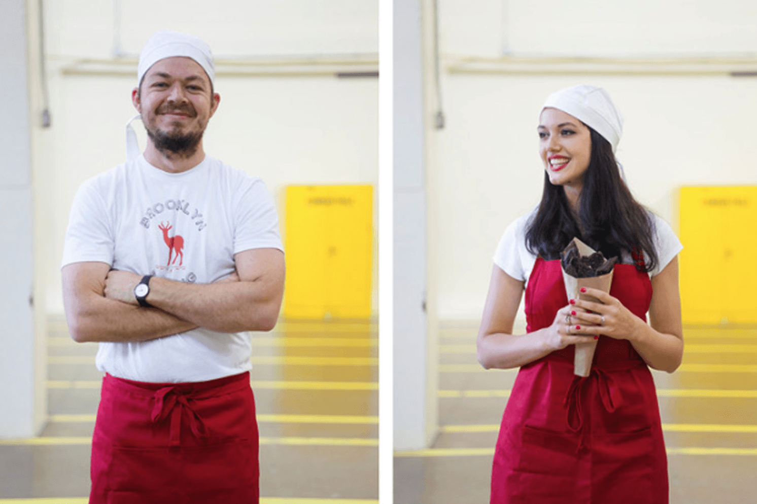 Ben and Emily, Brooklyn Biltong founders wearing branded shirts and red aprons, with one holding a paper cone of biltong.