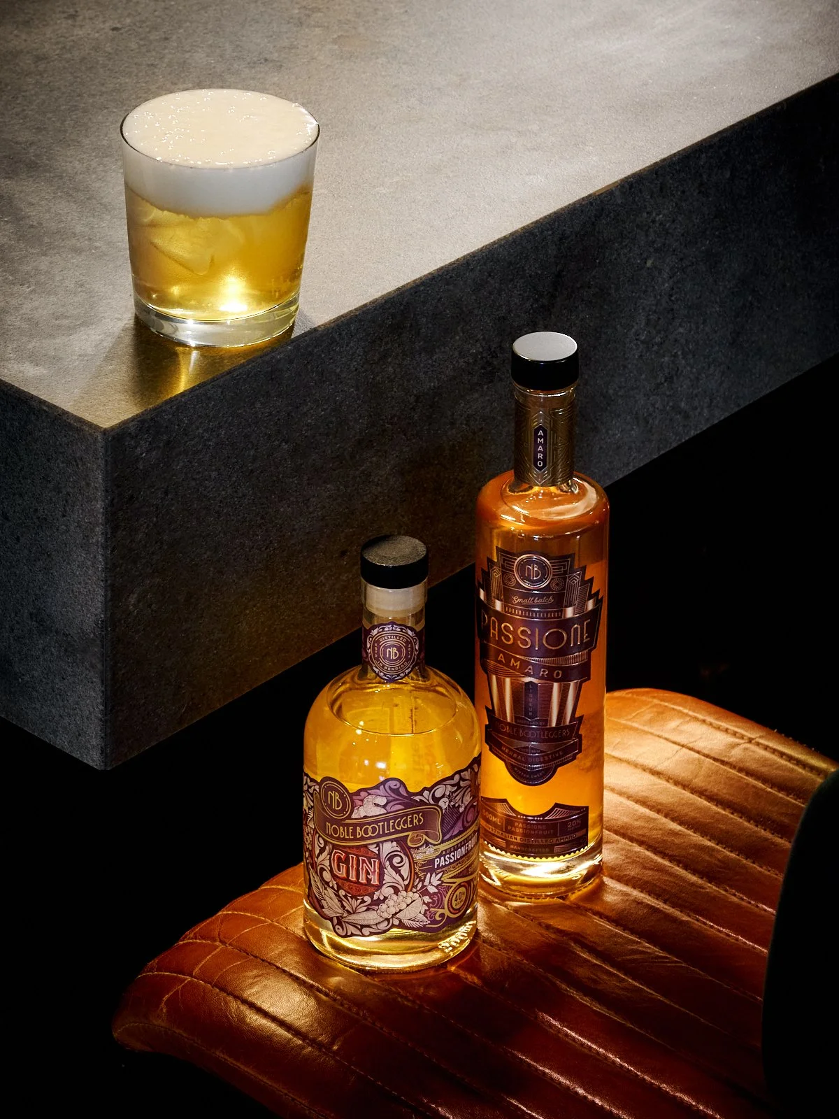 Noble Bootleggers Passionfruit Negroni with yuzu foam sitting on a bar. Passionfruit gin and Passione Amaro are sitting beside the cocktail.