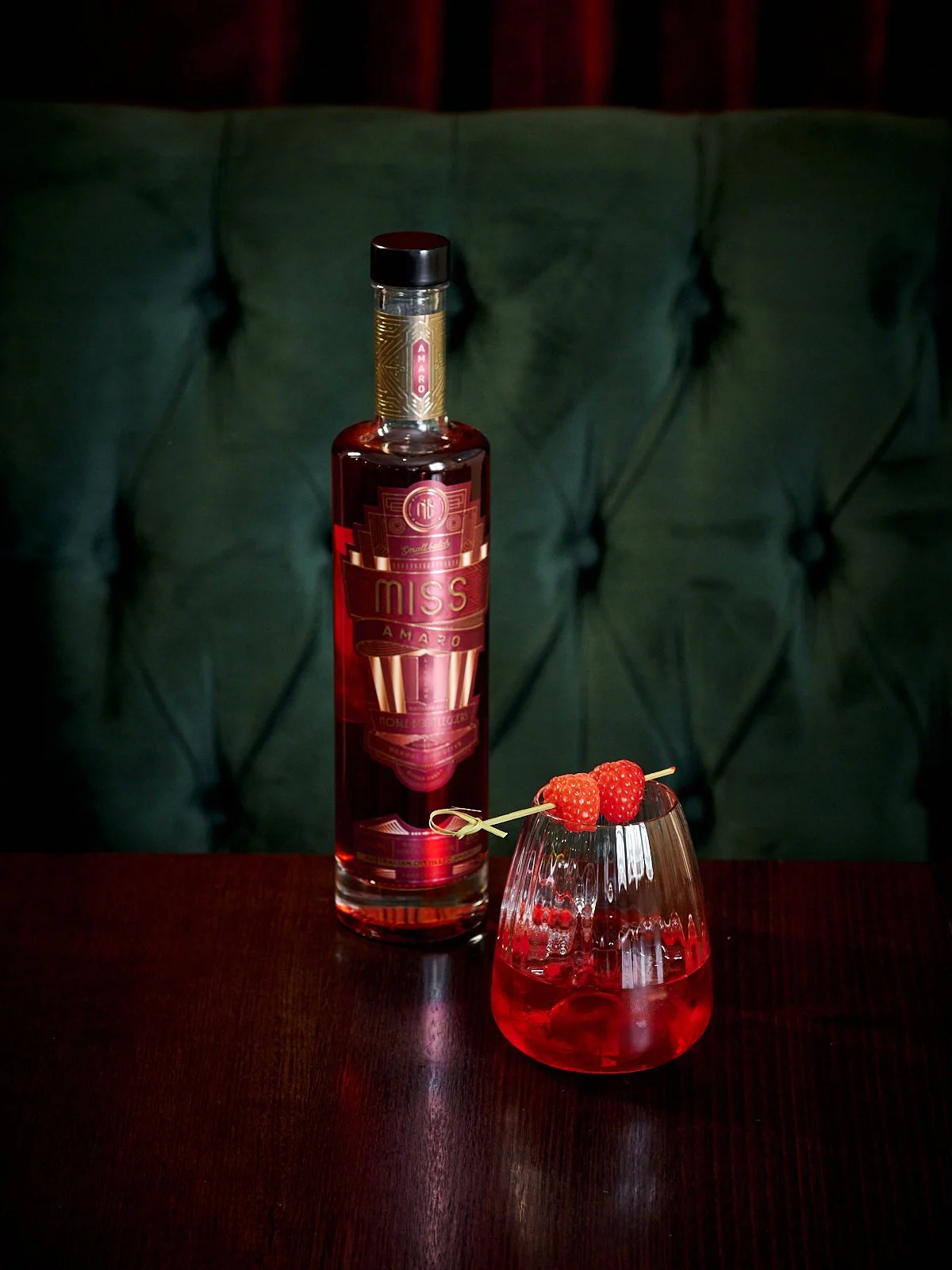 Noble Bootleggers Miss Amaro bottle accompanied by Miss Amaro served over ice, garnished with skewered raspberries