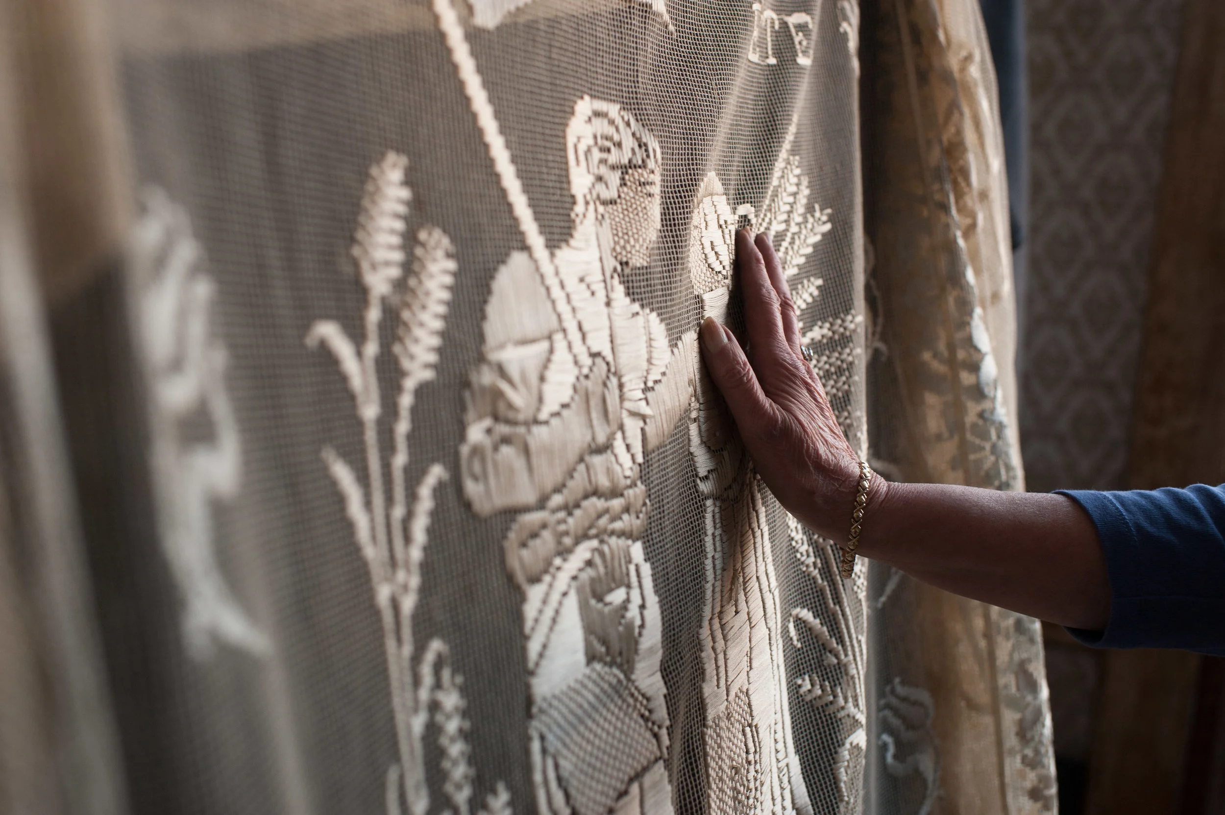 Charlotte reaches out to touch her favorite keepsake—a Sicilian bedspread hand-embroidered with fine ribbons. Her grandfather once traveled to Sicily to see his mother; he brought home a bedspread for each of his four daughters. In the center, the ribbons depict a farmer and his wife, and the word “summer” in Latin. It was the one thing Charlotte really hoped to inherit from her mother.