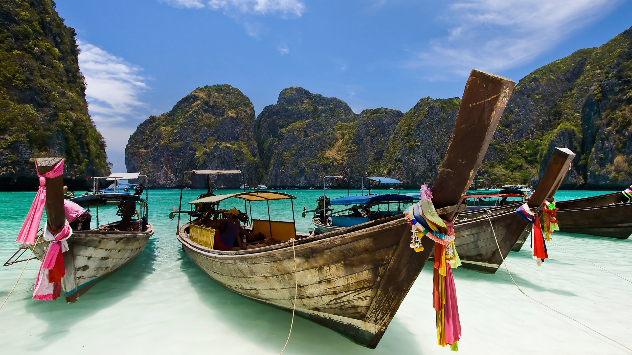 Long tail boats rest amongst limestone cliffs awaiting their next charter in Phang Nga Bay.