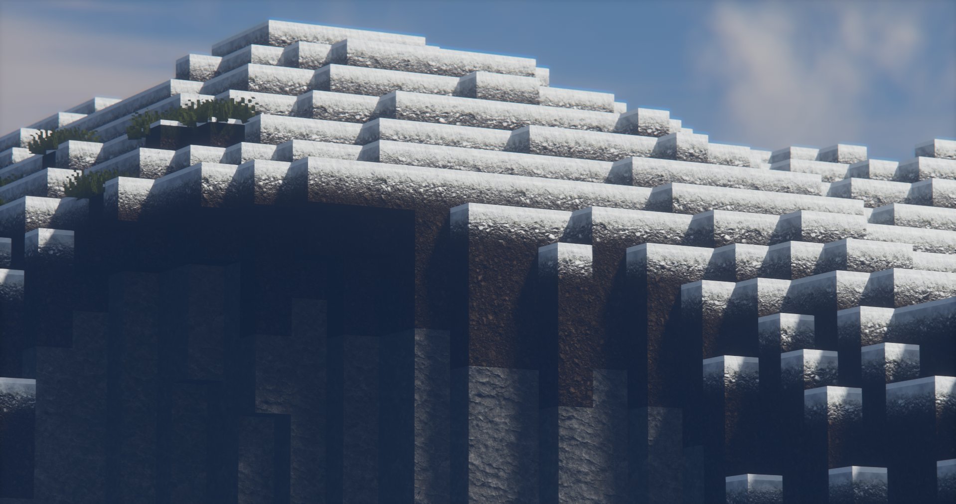 A stepped, pyramid-like structure made of layered, rectangular blocks with some greenery growing on the upper levels, set against a blue sky with clouds.